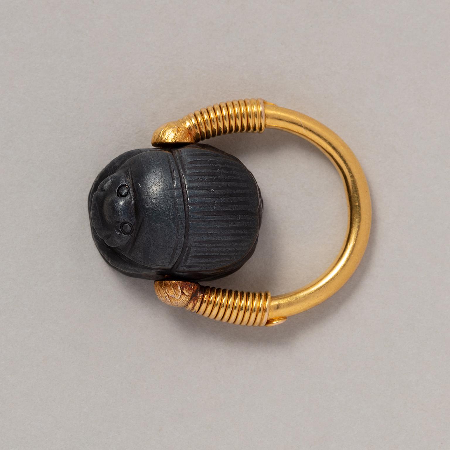 An 18 carat gold ring with a rotating stylised ancient Egyptian scarab carved from anthracite jasper, or other hard stone, France, French assay mark for gold and maker’s mark circa 1920.

ring size: 16 mm / 5.5 US
weight: 11.2 grams