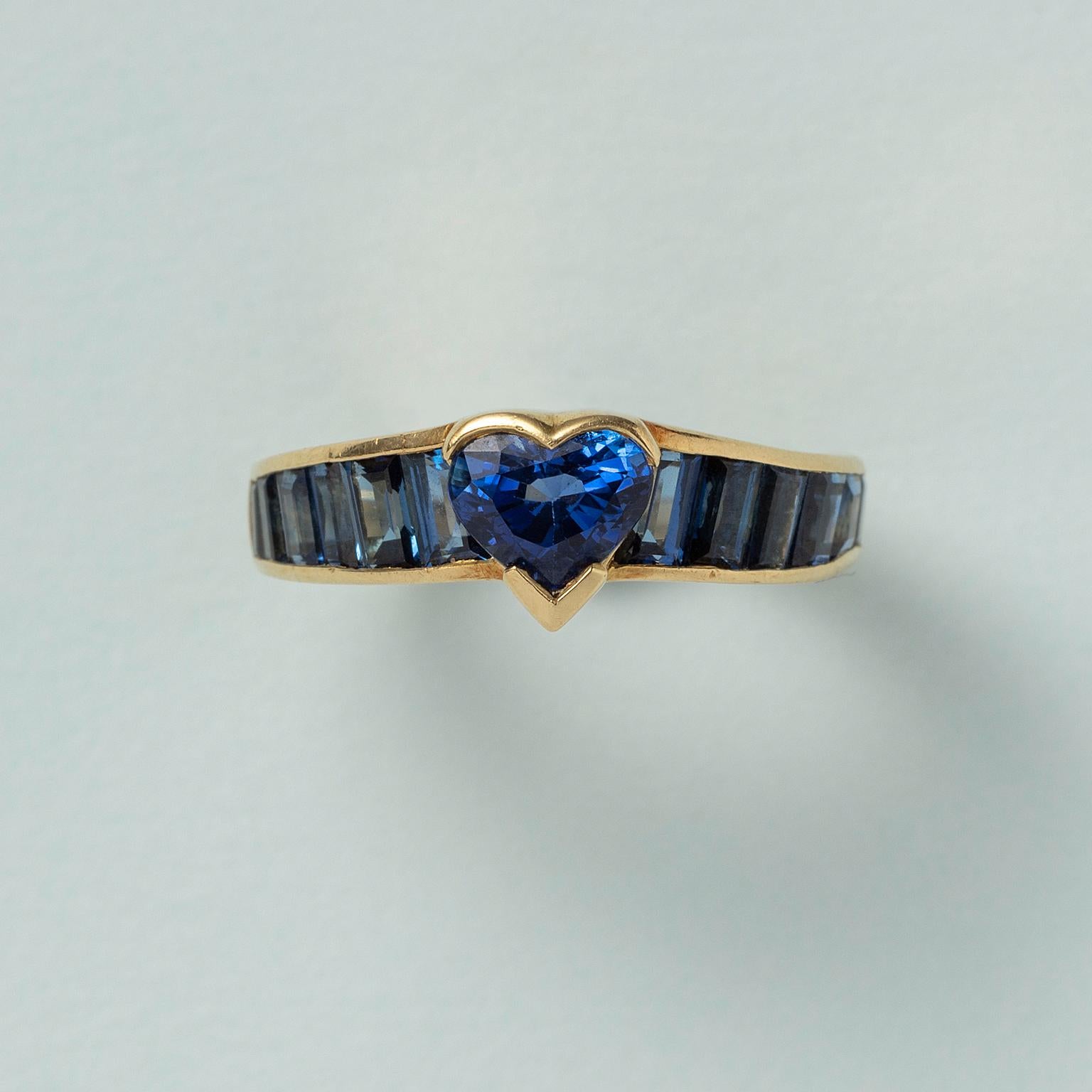 An 18 carat yellow gold ring set with a heart cut aapphire in the center with six baguette cut sapphires on each side, descending in size, France.

weight: 4.46 g
size: 14.75 mm / 4 US
width: 2.2 - 6.5 mm