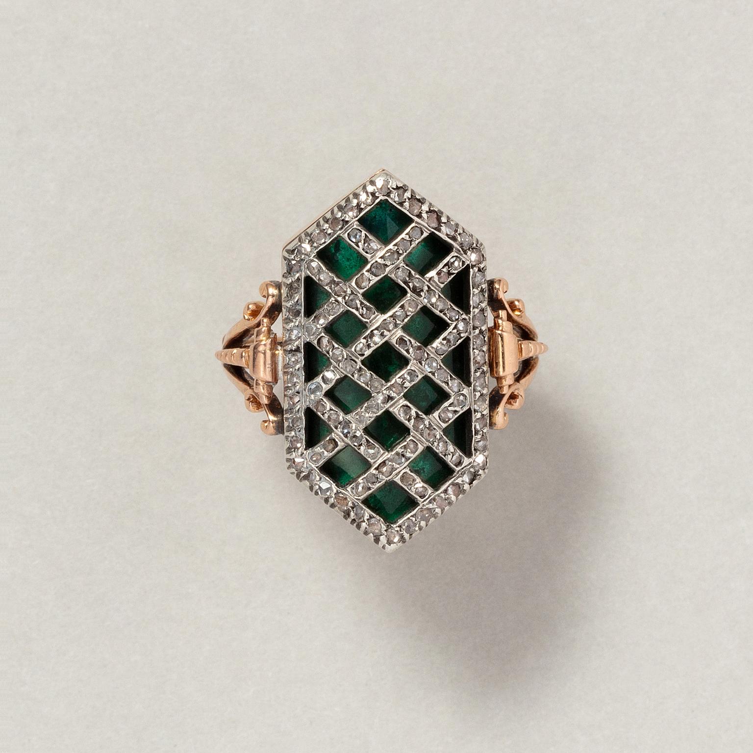 An 18 carat rose gold and ring with a hexagonal concave element with dark green, transluscent glass over which a silver diagonal grid set with rose cut diamonds, the shank is florally engraved and with a three forked hoop with scrolls, the shank has