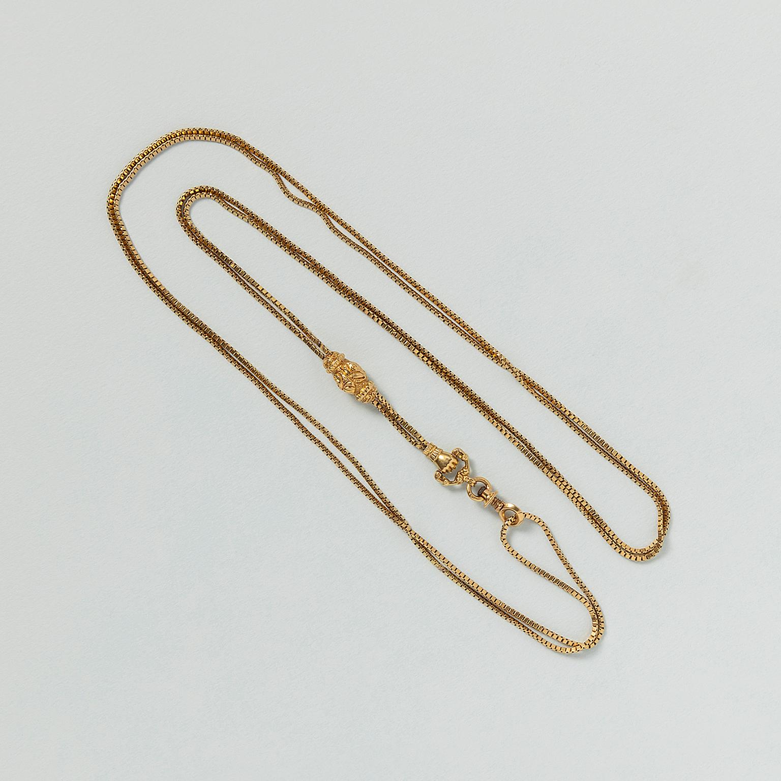 An 18 carat yellow gold watch chain with a swivel clasp and a very richly decorated gold sliding bead and a hand holding a clasp. The central slide is decorated with shells. One hand holds the rotating clasp that can be screwed up to open. The lock