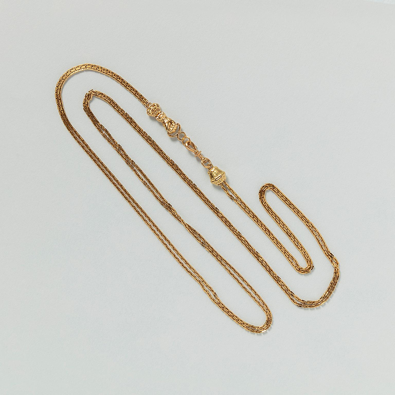 An 18 carat yellow gold watch chain necklace with rectangular links and a richly decorated gold sliding bead and an opening lobster clasp at the end and a hand holding a clasp and the other end of the lock, France, circa 1850.

weight: 19.16