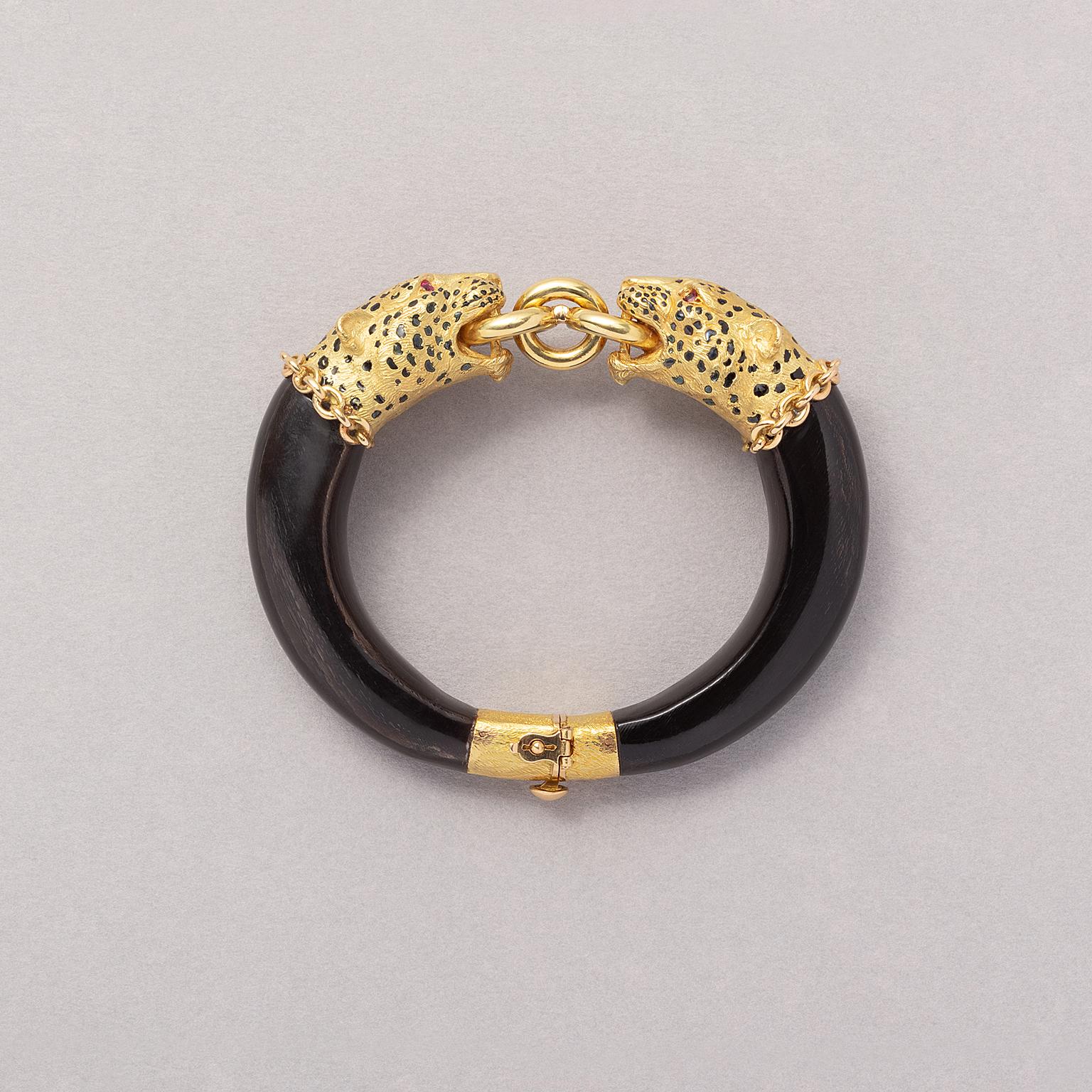 An 18 carat yellow gold panther bangle consisting of two elements that are connected with a single mobile gold ring that are held from by the gule of two panther heads with round facetted ruby eyes and their spots in black enamel with French assay