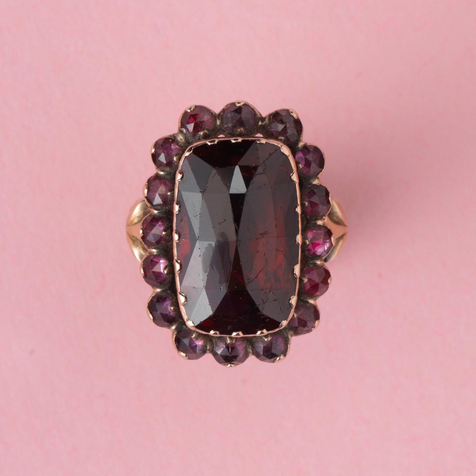An 18 carat gold ring with a large rose cut rhodolite garnet and a border of small round rose cut garnets, all set on gold foil, marked with the tête de coq, Perpignan, France, circa 1820.

weight: 6.97 grams
ring size: 15.75 mm