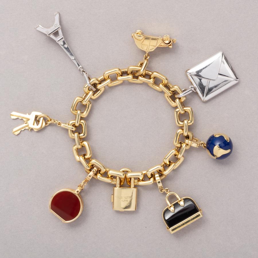 An 18 carat yellow gold oval link bracelet with seven different travelling souvenir charms: a padlock and keys, a blue enamelled globe, the Eiffeltower in white gold with small brilliant cut diamonds, an old Tinsnail (Citroën 2CV) with yellow