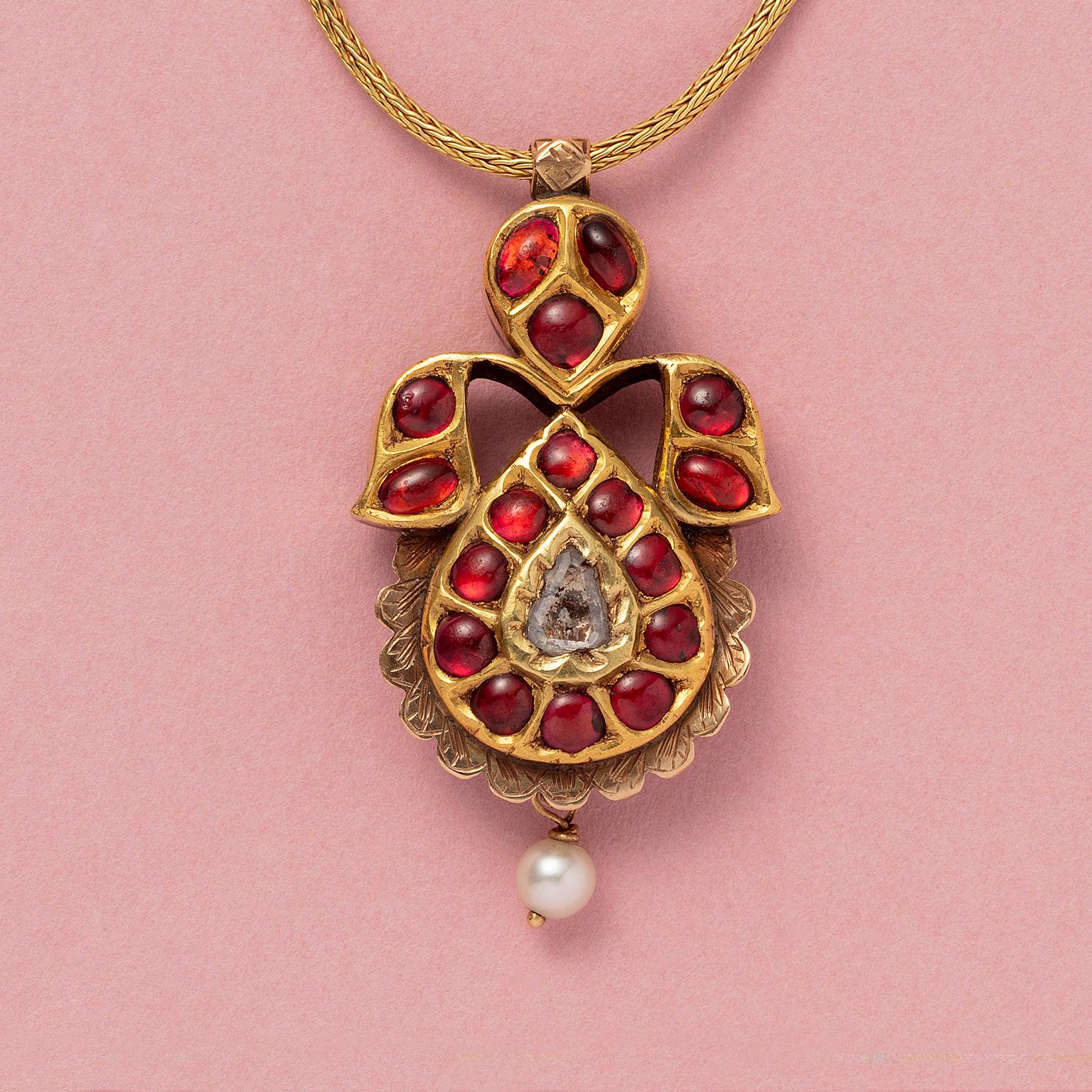 An 18 carat yellow gold amulet or padak pendant from India set with cabochon cut garnets foil set and a diamond in the middle, the back is fully engraved with floral decorations, with a little pearl, with an 18 carat gold necklace and 14 carat gold