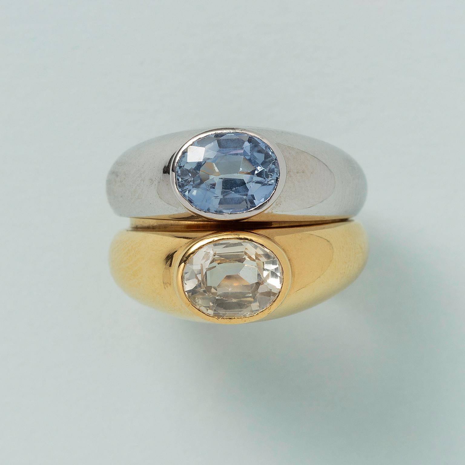 A set of two 18 carat gold rings, one white gold and one yellow gold, that fit into each other and can be worn together or separately, each is set with an oval-facetted sapphire, one slightly blue-er than the other, (app 3 carats in total), marked