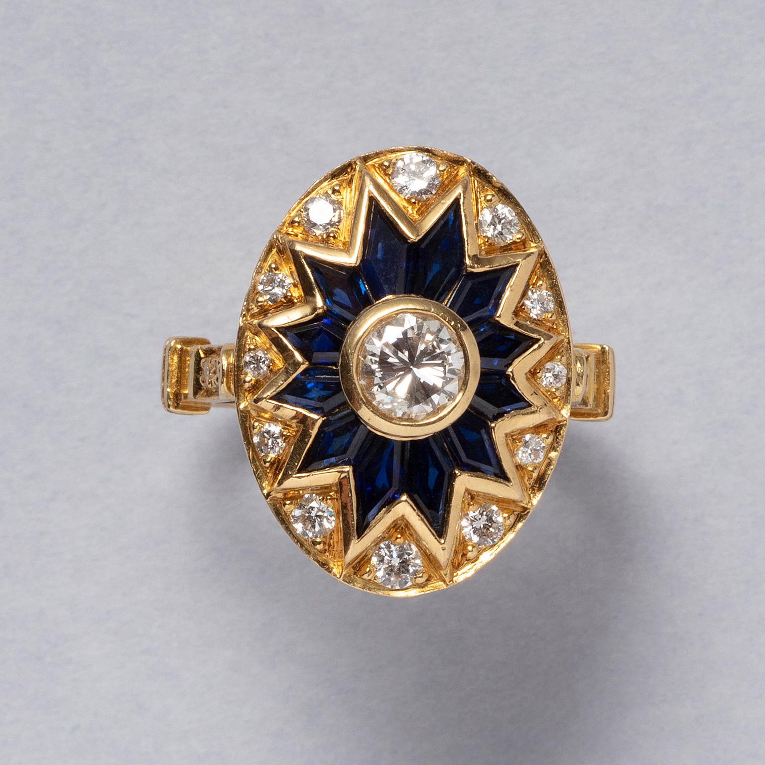 An 18 carat yellow gold ring, with a gold oval on top. A stretched, twelve point star in the center, set with a brilliant cut diamond in the heart surrounded by callibré cut sapphires in a star. Between every point a smaller brilliant cut diamond