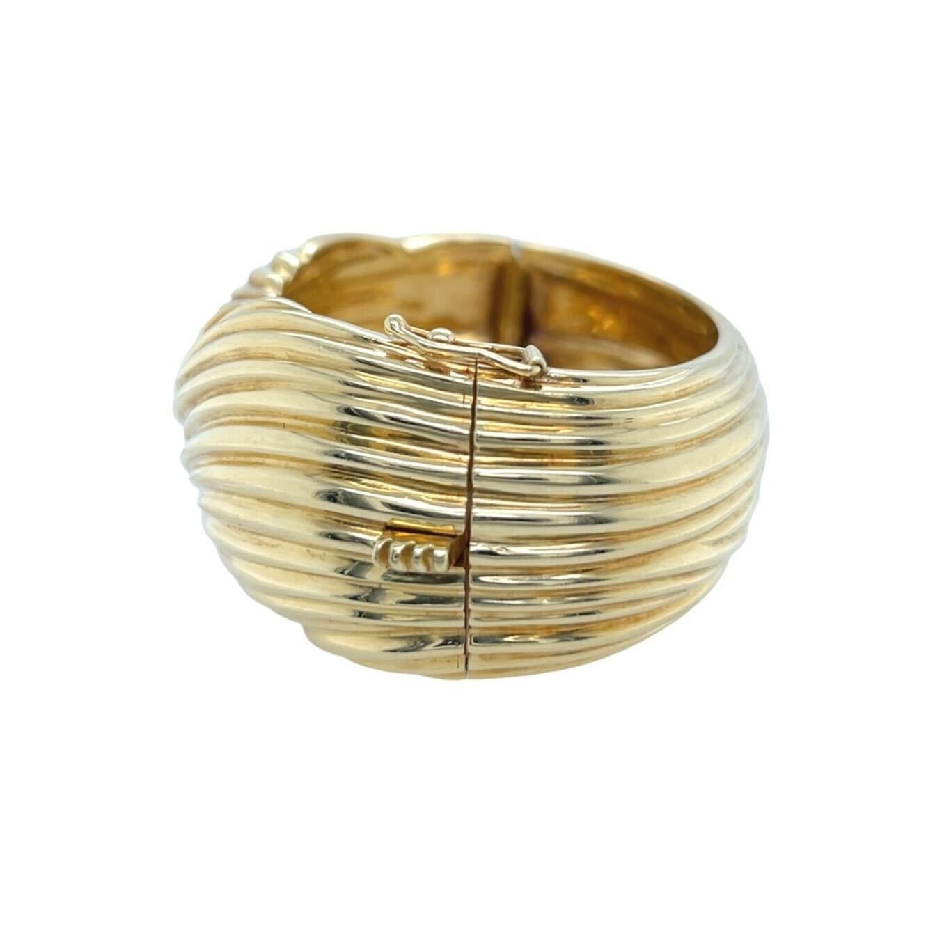 An 18 karat yellow gold bracelet.  Designed as subtly tapering hinged cuff bangle displaying interlocking waves of striated gold.  Inner circumference approximately 6 1/4 inches, width at widest point approximately 1 1/4 inches.  Gross weight