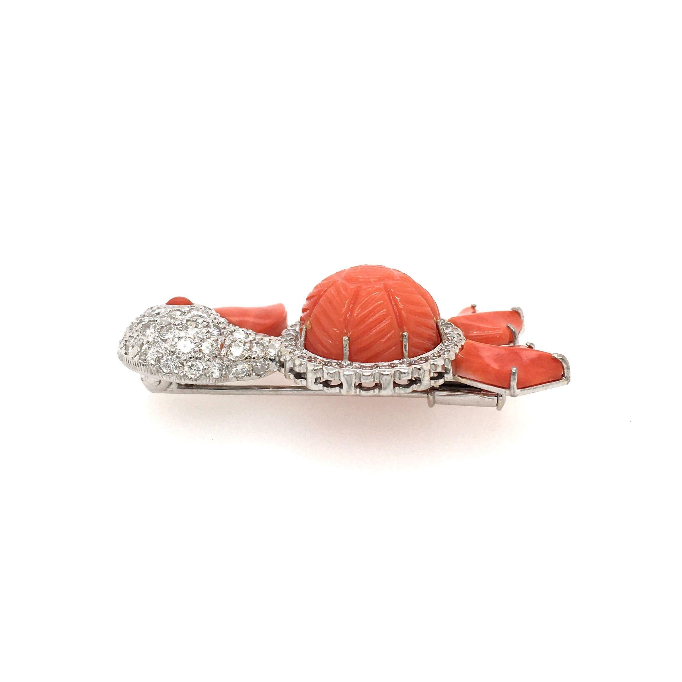 An 18 karat white gold, diamond and coral duck brooch. Designed as a pave set diamond duck, centering a carved coral belly enhanced by coral beak, feet and eye. Seventy (70) diamonds weigh approximately 1.40 carats. Length is approximately 1 5/8