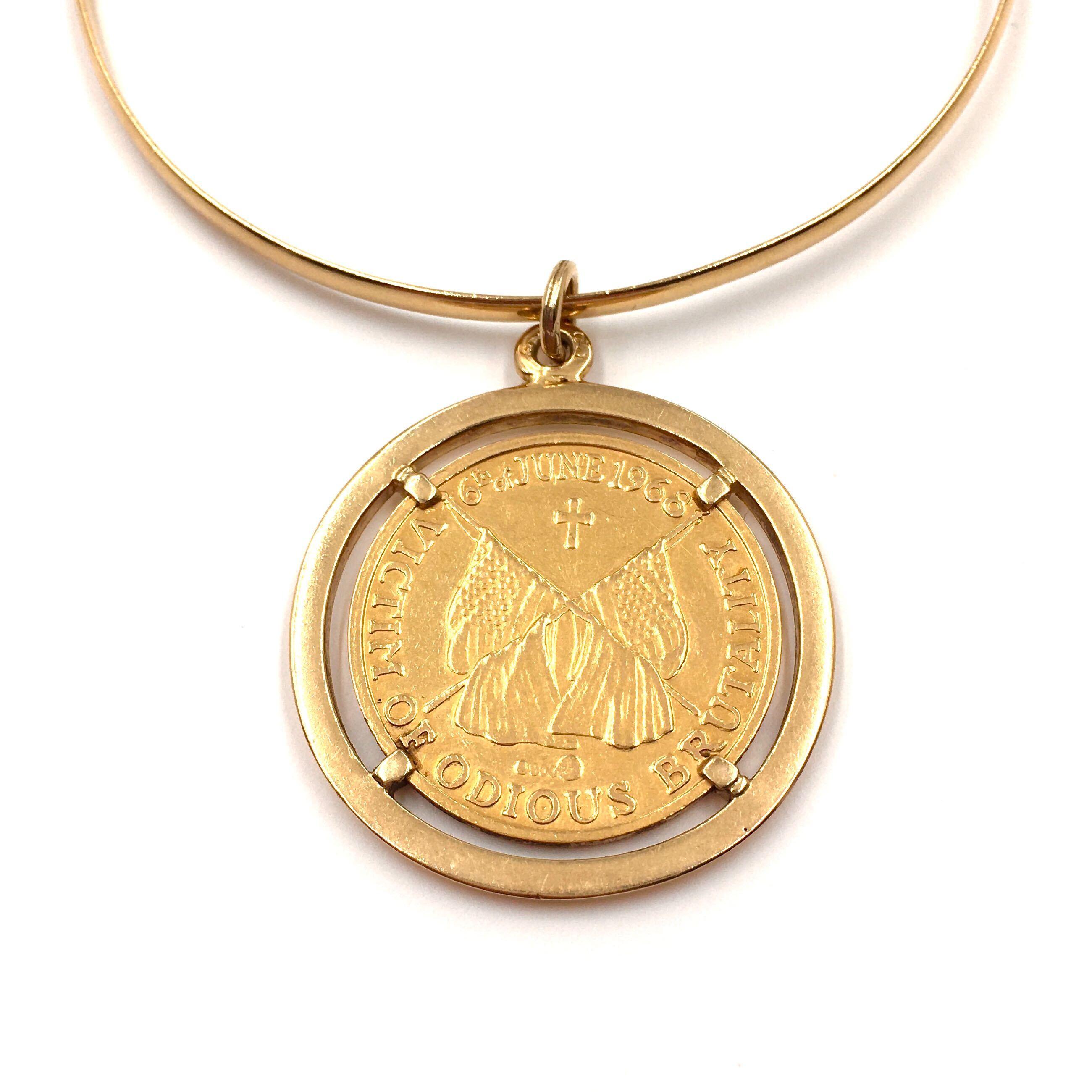 An 18 karat yellow gold bracelet with 22 karat yellow gold coins. Designed as a bangle, suspending two (2) commemorative coins, one depicting President John F. Kennedy, engraved in German ‘Wir alle haben ihn verloren, 22 November 1963, translated to