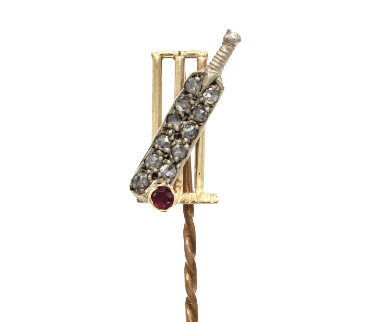 An 18 Kt yellow and white gold, diamond and ruby stick pin modeled as a cricket bat and ball in front of a set of stumps.
The white gold cricket bat set with eleven diamonds and the ball set with a ruby, all in front of a set of a set of yellow gold