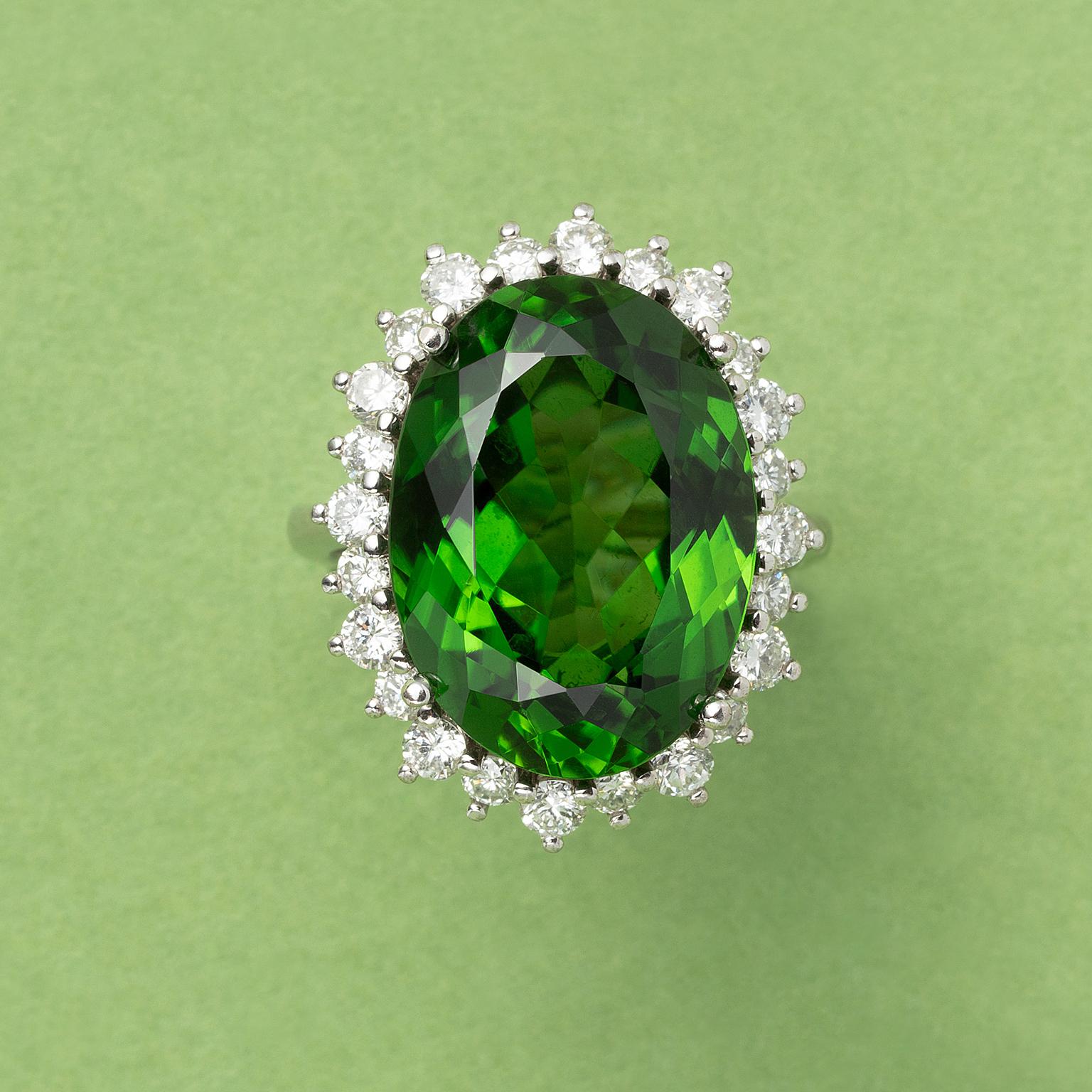 An 18 carat white gold ring set with a large oval facetted green tourmaline (app. 14.00 carat with an entourage of brilliant cut diamonds (0.05 carat each, colour FG, Vs, gem report AEL-Arnhem).

weight: 11.5 gram
ring size: 16.25 mm