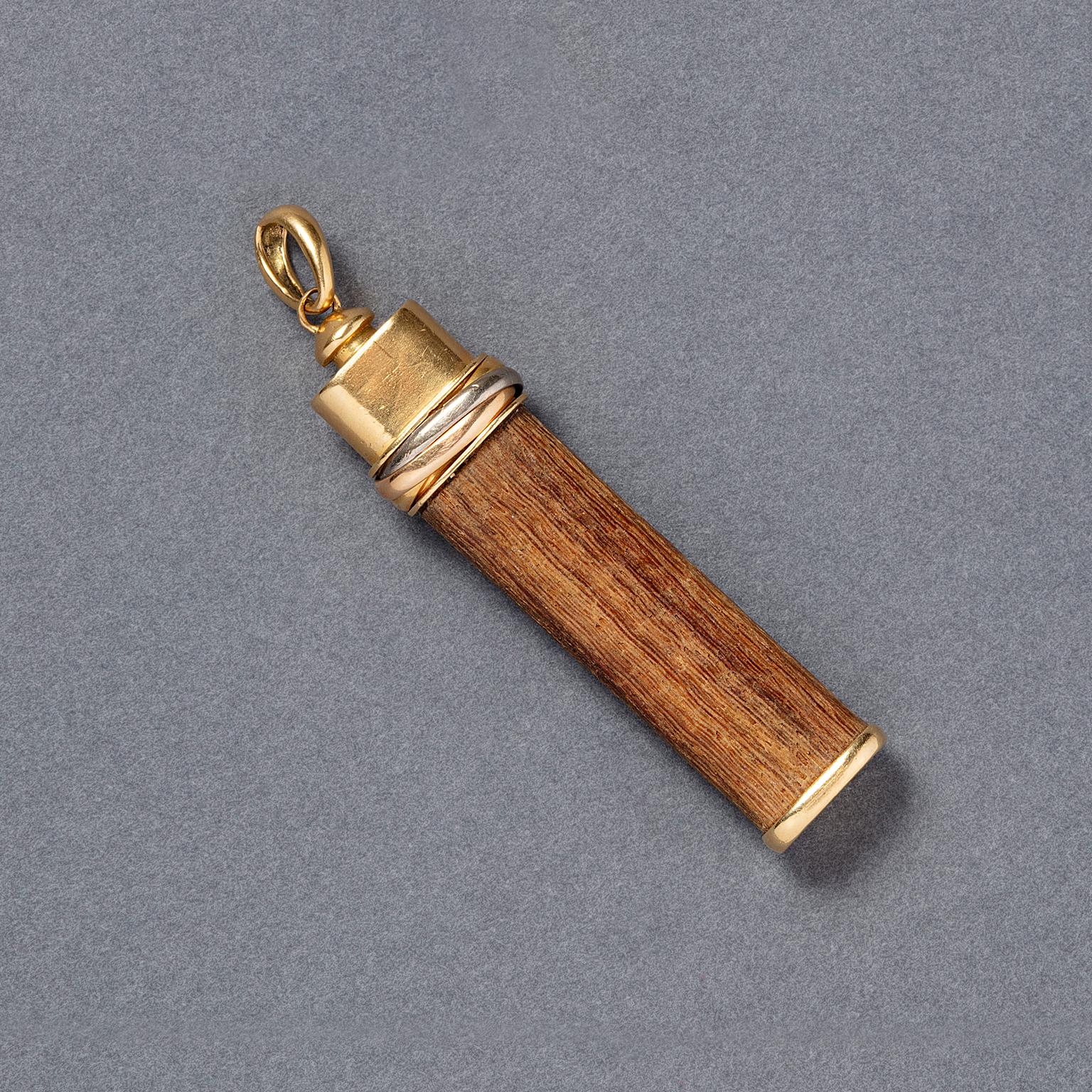 An 18 carat gold lucky “touch wood” or “toucher du bois” Trinity pendant. A long piece of wood with a tri-color gold band and an oval hoop, signed and numbered: Cartier, circa 1980.

weight: 8.33 g
dimensions charm: 6 x 1.2 cm