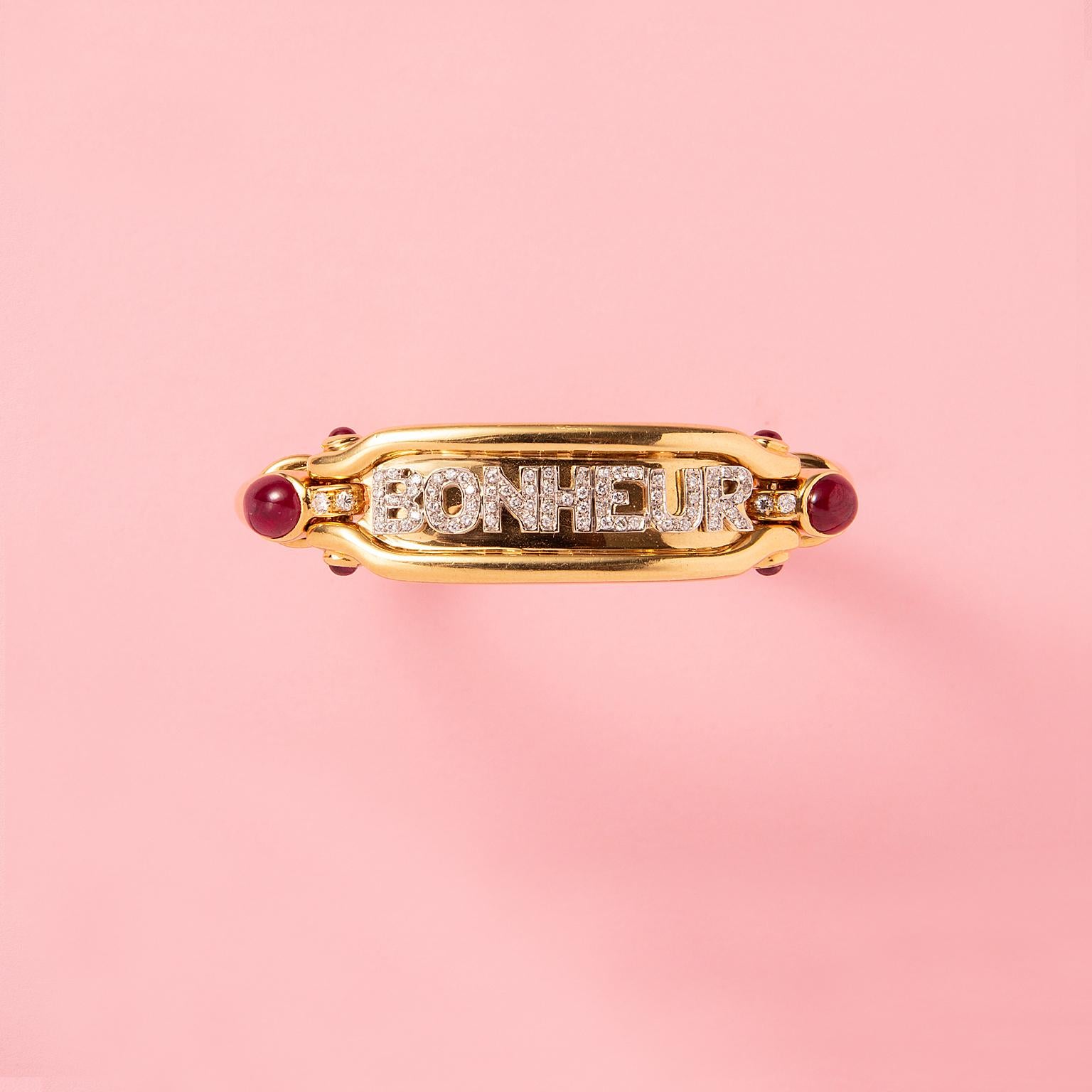 Armband aus 18 Karat Gelbgold mit der Aufschrift BONHEUR in Weißgoldbuchstaben, besetzt mit kleinen Diamanten im Brillantschliff (ca. 0,70 Karat), mit einem ovalen Rubin im Cabochon-Schliff auf den Schultern des Armbands neben dem Armband und mit