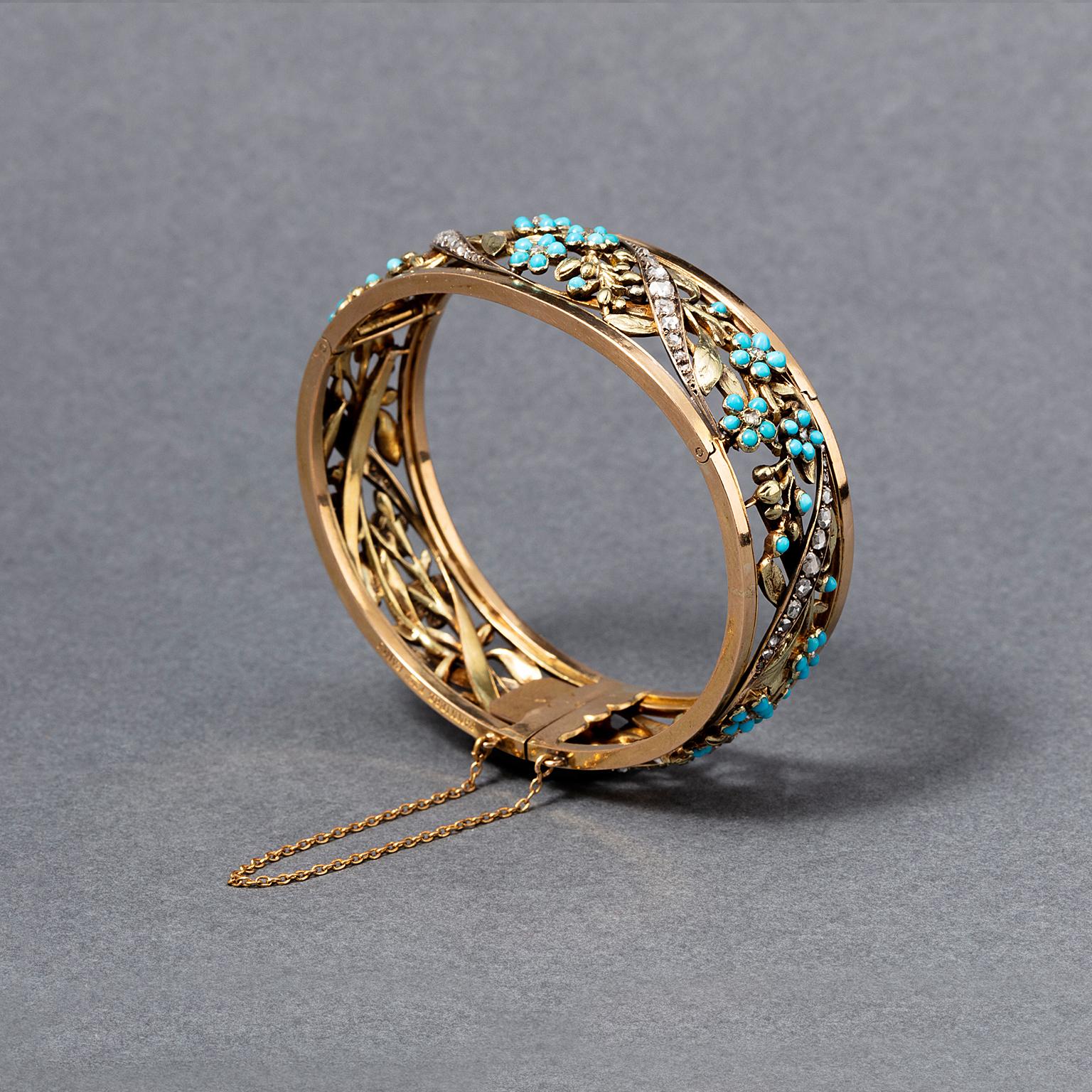 An 18 carat warm yellow gold and white gold bangle bracelet that opens at the back with two hinges, with an open worked decoration of forget-me-nots and leaves, set with turquoise and rose cut diamonds, with a ribbon weaved through it set with rose