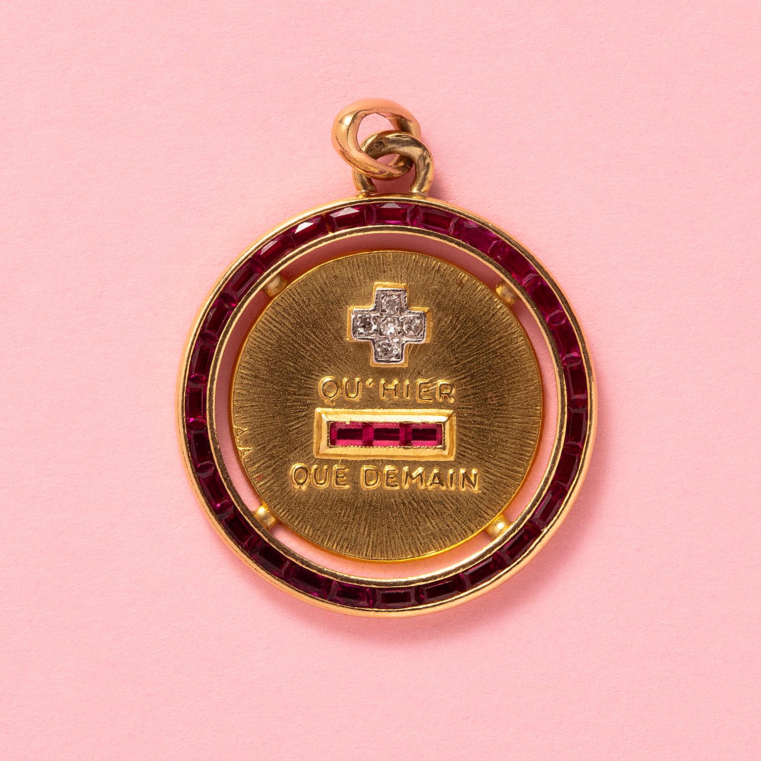 An 18 carat yellow gold round love charm with a border of synthetic rubies and a plus sign in the middle with five 8-cut diamonds and the text 