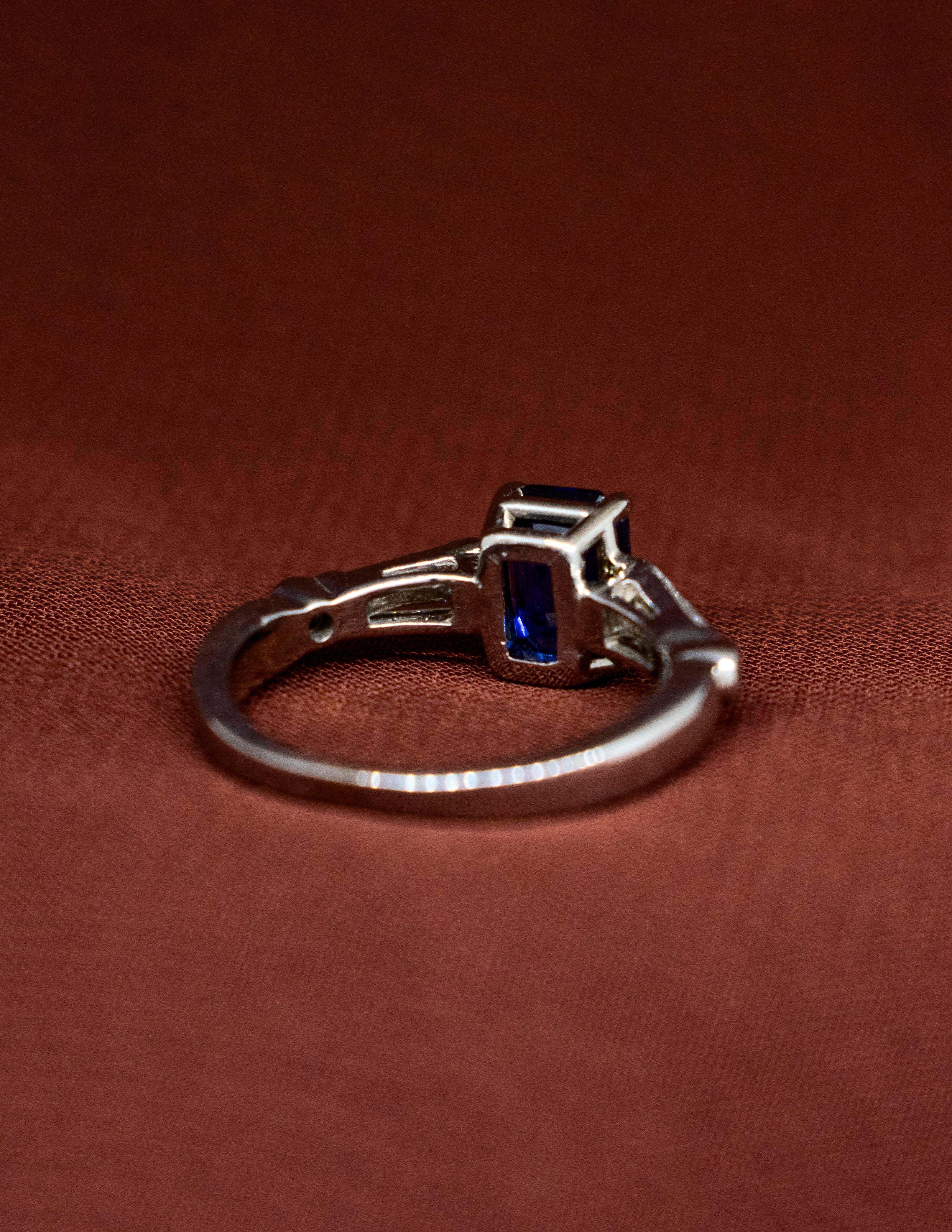 A Ladies Ring made of 18k White Gold mounted with a Deep Blue, Emerald Cut Sapphire and Baguette Diamonds. The center stone is a natural, earth-mined sapphire. It is an octagonal step cut (Emerald Cut) weighing approximately 1.60 carats, grading