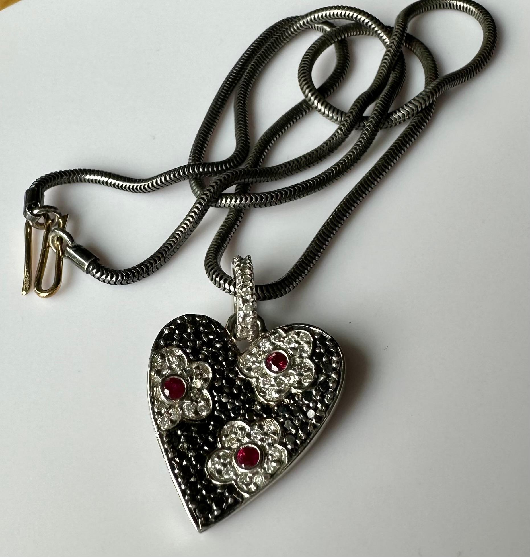 An 18kt White Gold Pendant set with Rubies & Diamonds.
This lovely 18kt White Gold Heart Pendant is pave set with 3 small accent Rubies and many Black and White Diamonds. The Pendant’s bail is channel set with tiny white diamonds adding a lovely