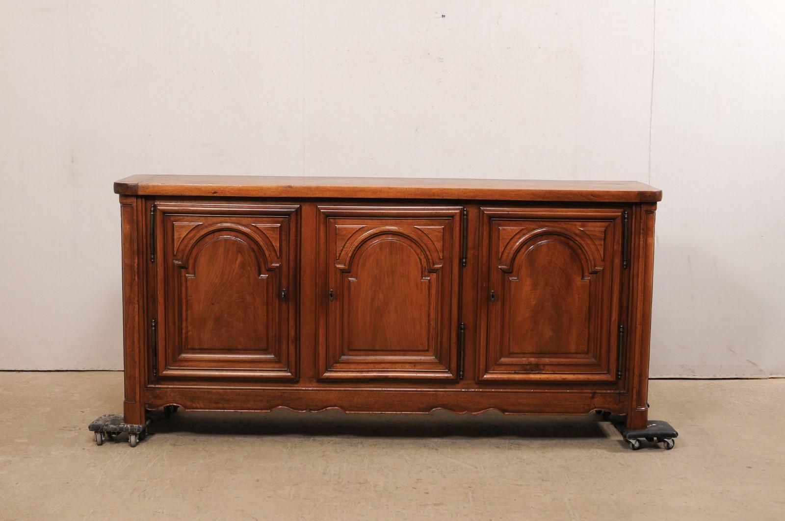 A French carved-wood, three-door buffet cabinet from the 18th century. This antique cabinet from France, which is approximately 7.5 feet in length, features a rectangular-shaped top, with softly rounded front corners, which rests above a case which