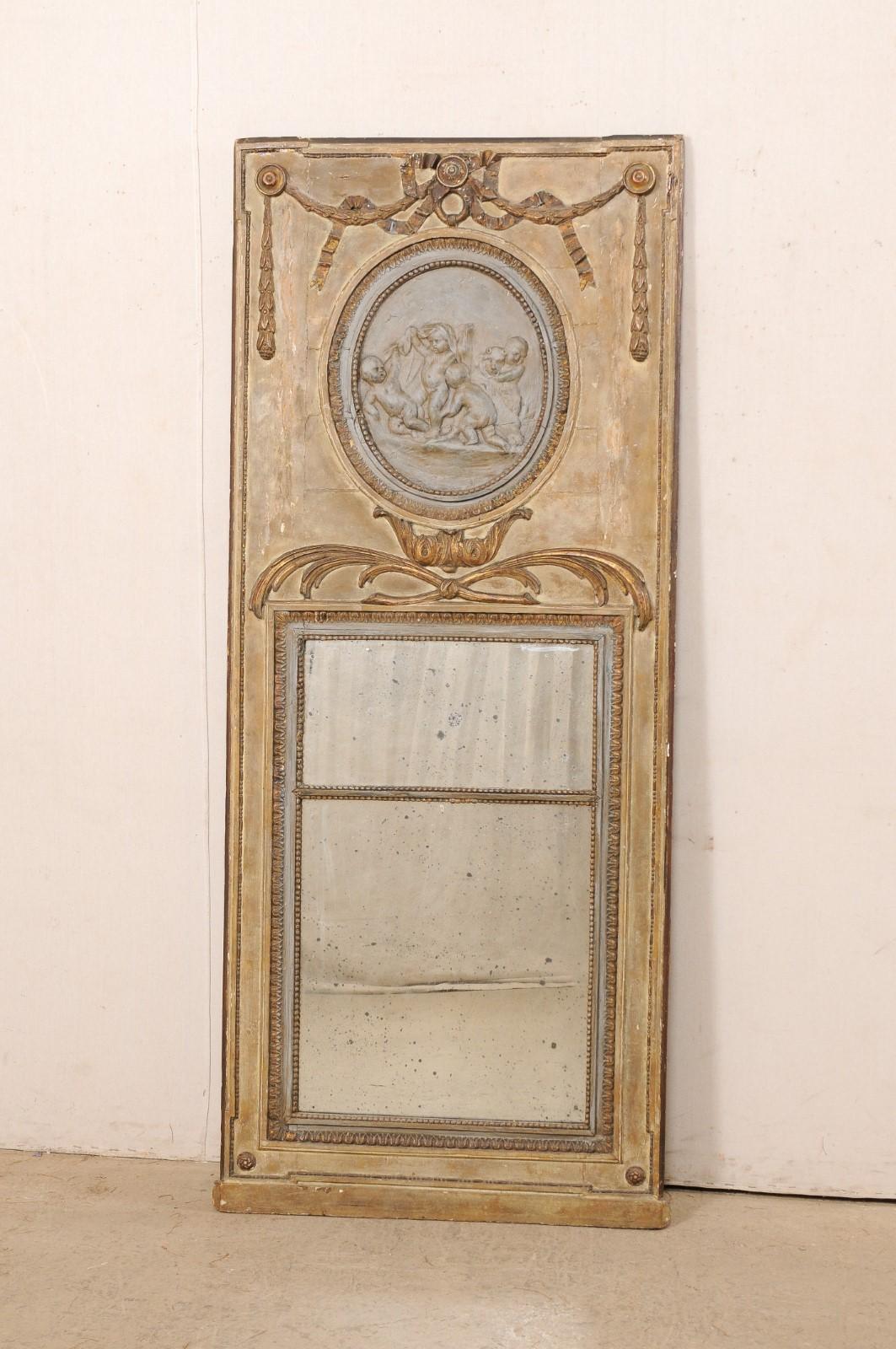 A French neoclassic carved and painted wood trumeau mirror from the 18th century. This antique mirror from France has the tall rectangular-shape, typical of trumeau design, with wooden top section adorn with neoclassical carved bow-ties and garland