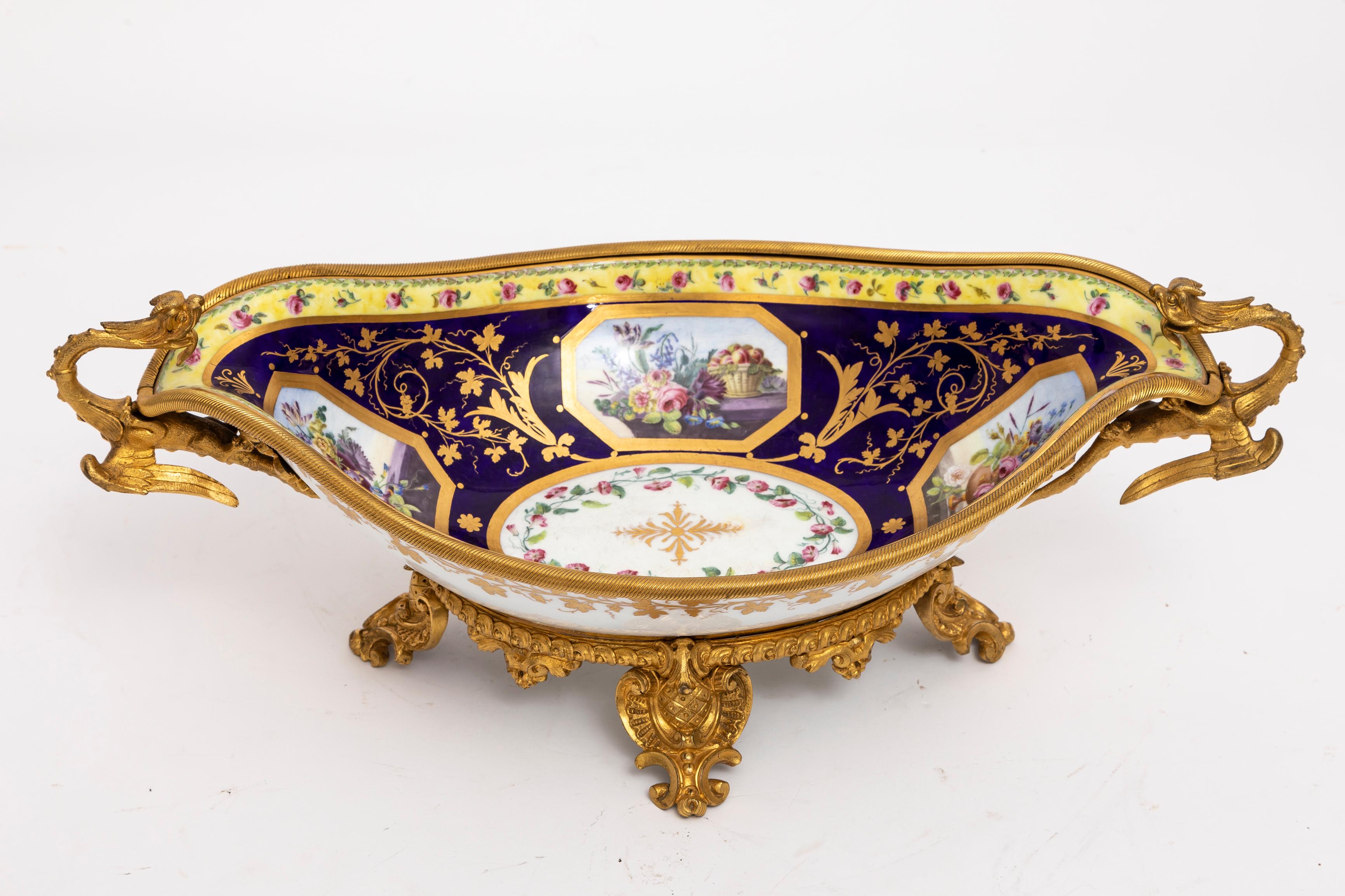 Cet exquis centre de table en porcelaine de Sèvres du XVIIIe siècle peint et décoré par Jacques Pierre, orné de ravissantes poignées de dragon en bronze doré du début du XIXe siècle et de montures en bronze doré de la plus haute qualité, est un