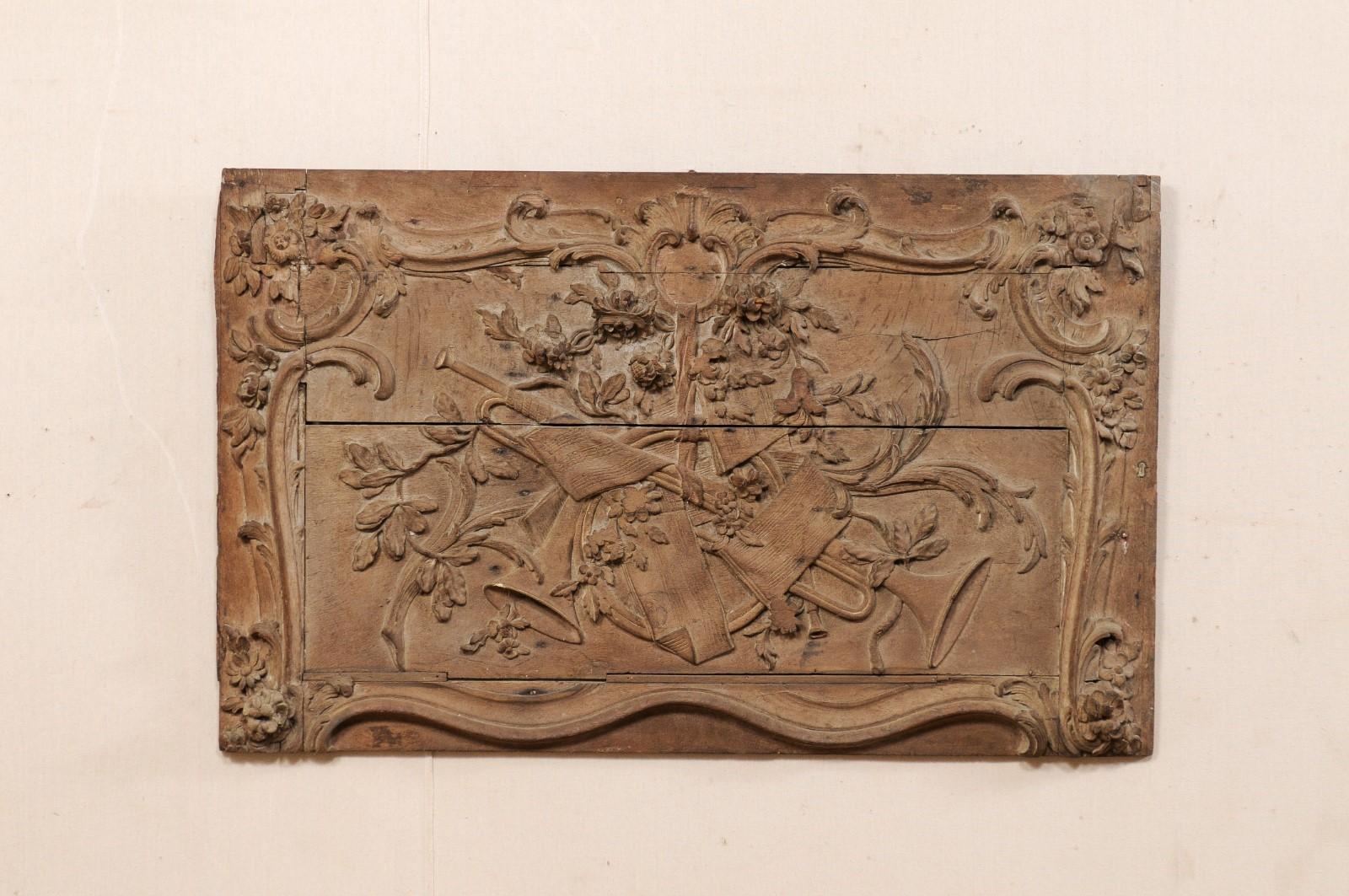 A French musically inspired carved-wood wall plaque from the 18th century. This antique wall decoration from France is rectangular in shape and has raised carvings which depicts a musical motif with horn instruments and sheet music at it's center,