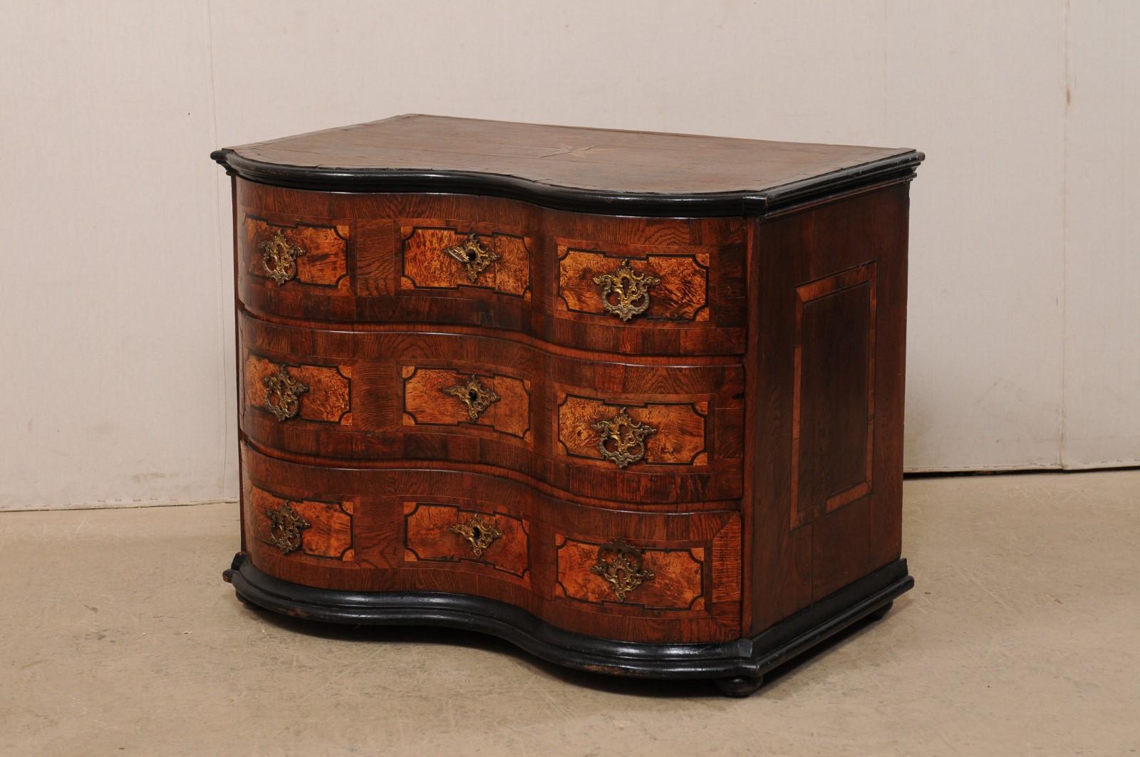 An Italian serpentine commode with exquisite marquetry and inlay designs from the 18th century. This antique chest from Italy, with curvy serpentine top and body, features a stunningly rhythmic design of marquetry and inlays adorning the drawer