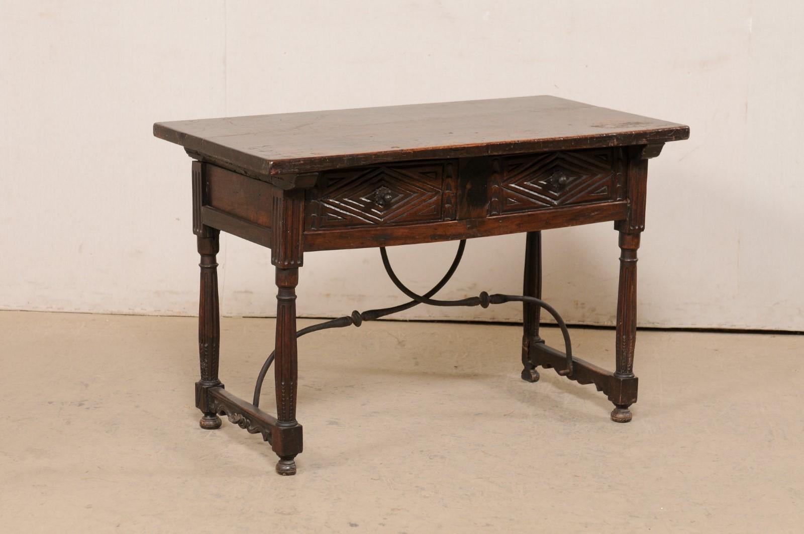 An Italian two-drawer table with iron stretcher from the late 18th century. This antique walnut table from Italy has a rectangular-shaped top, which overhangs the apron below which houses a pair of drawers at one long side, which are carved in a