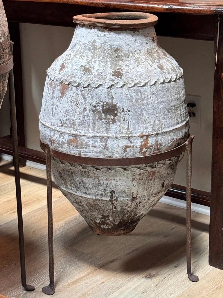 An 18th century Anatolian terracotta storage jar with applied wavy banding and remnants of old whitewash, suggesting long use and age. Originally for olive oil or grain, now a sculptural element with striking surface texture. Presented in a custom
