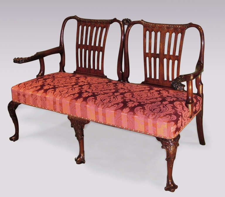 A rare mid-18th century mahogany double-chair settee in the manner of Giles Grendey having acanthus carved top rails joined with central coronet above wide pierced slats. The settee with well-carved set-back lions head arms, supported on acanthus