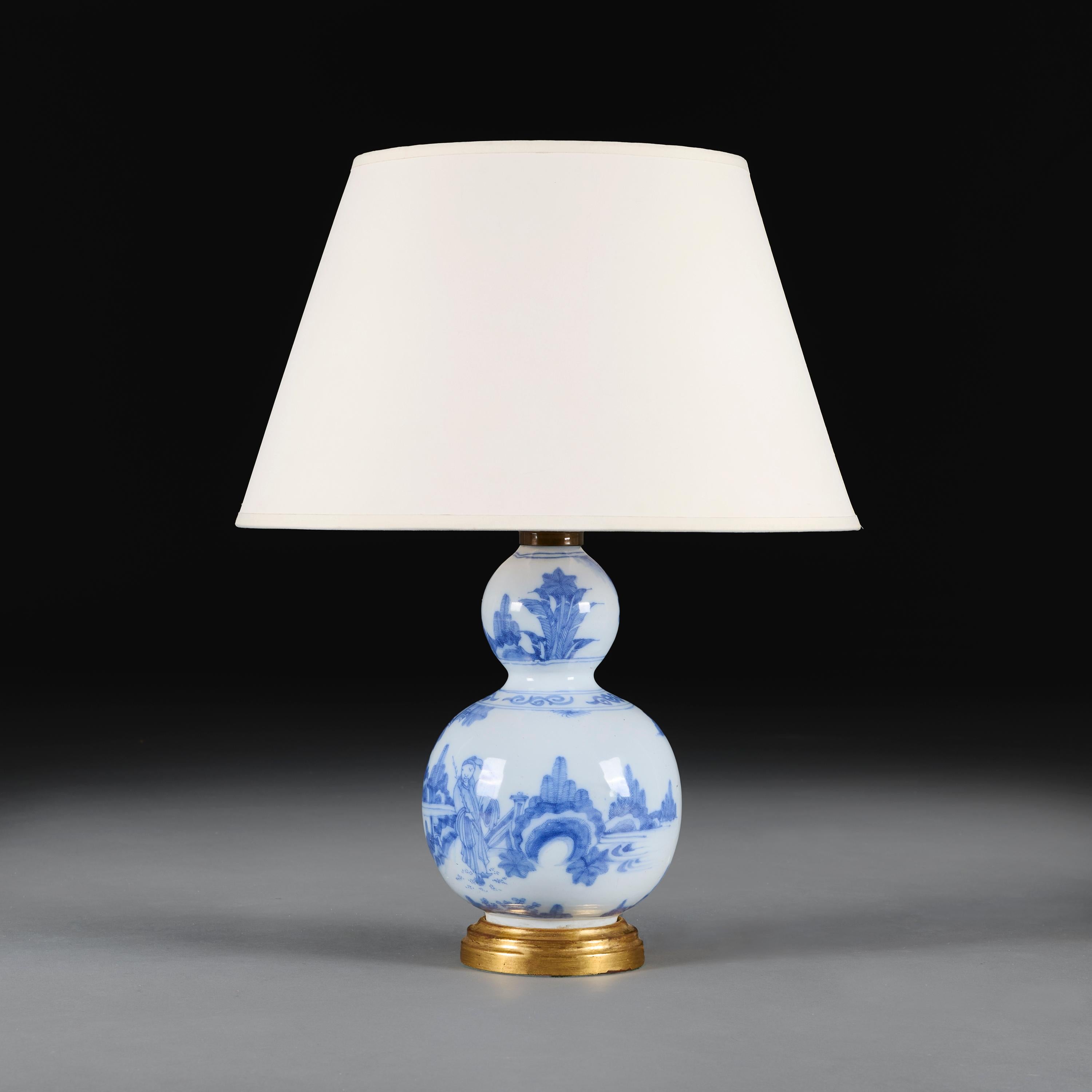 China, circa 1780

A late eighteenth century double gourd lamp, decorated with blue painted figures wandering through a traditional garden on a white ground, now mounted as a lamp on a giltwood base.

Height 29.00cm

Diameter 17.00cm

Please