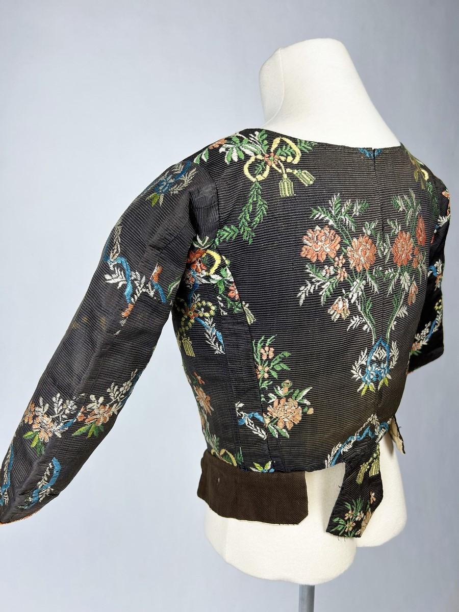 Circa 1750

France

Caraco or supple body in brown brocaded French faille, Louis XV period. Unstuffed caraco à la négligé, small basques with pet-en-l'air, three-quarter bent sleeves trimmed with a salmon silk ribbon. Unbleached linen lining (slight
