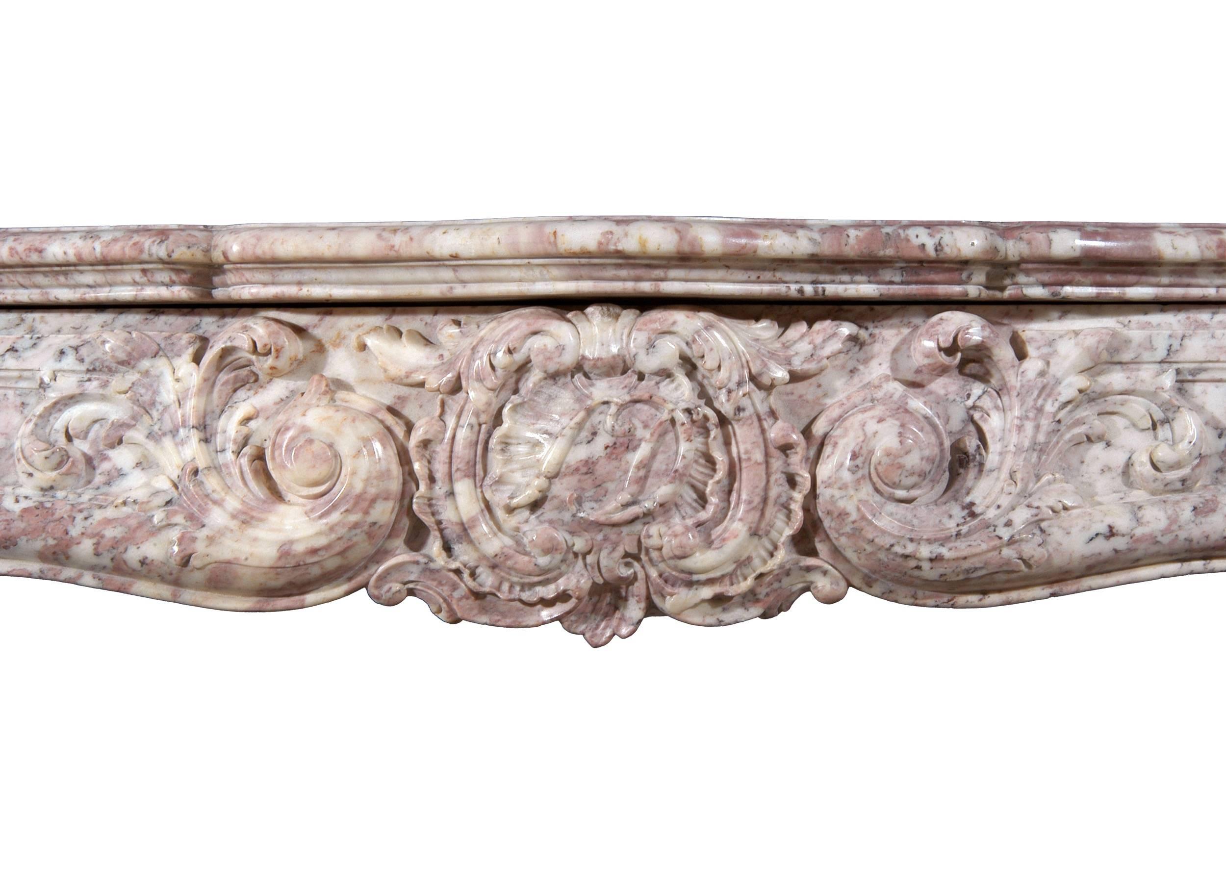 An ornately carved 18th century (circa 1760) French Louis XV Rose Boreal marble fireplace, the frieze with shell, scrolls and leaves, the shaped jambs of reeded form with shells and scrolls, and with unusual carved and panelled inner section,