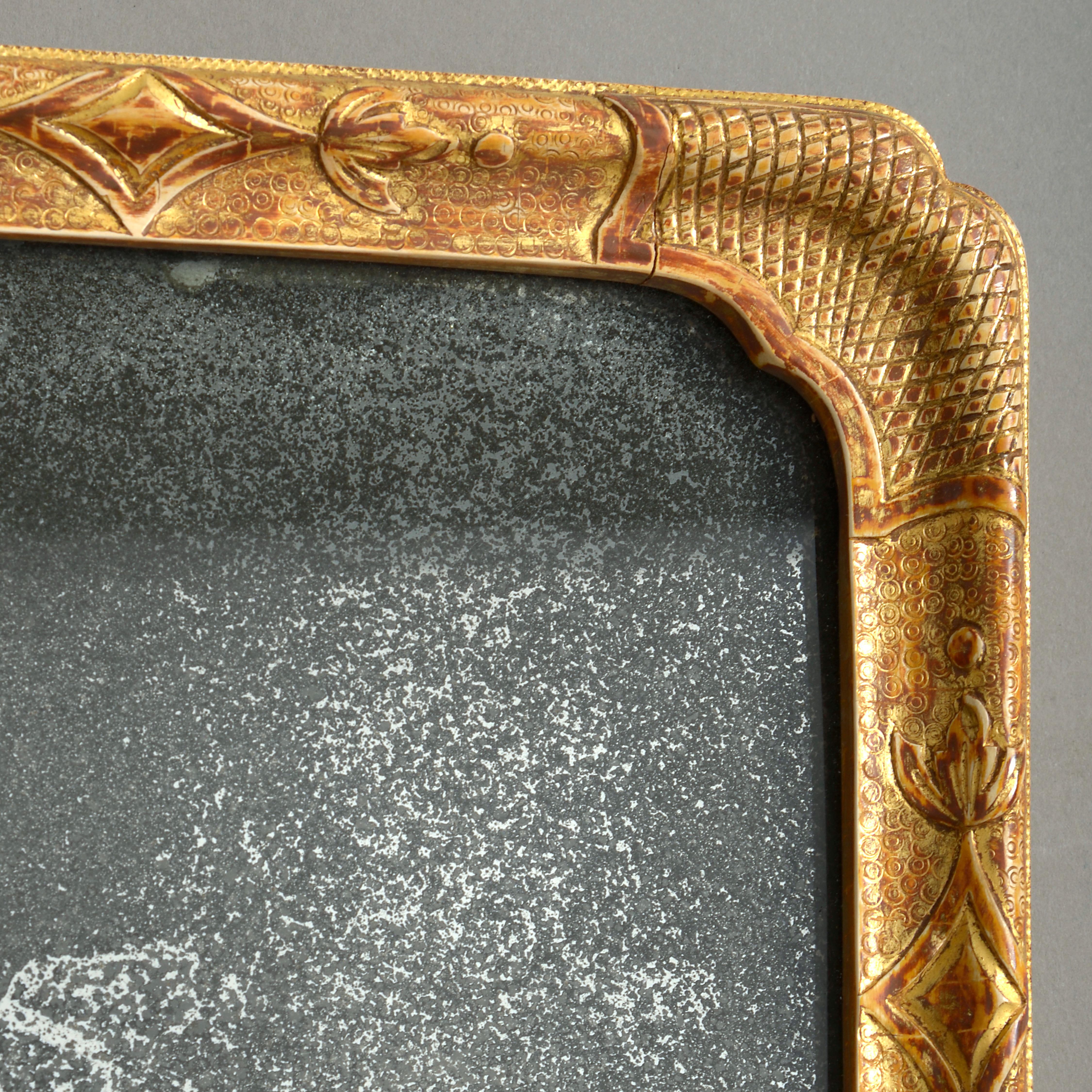 An early 18th century George I Period girandole mirror, the mercury glass plate held within a carved gilt gesso mirror of rectangular form, having re-entrant corners and supporting two brass candle arms.