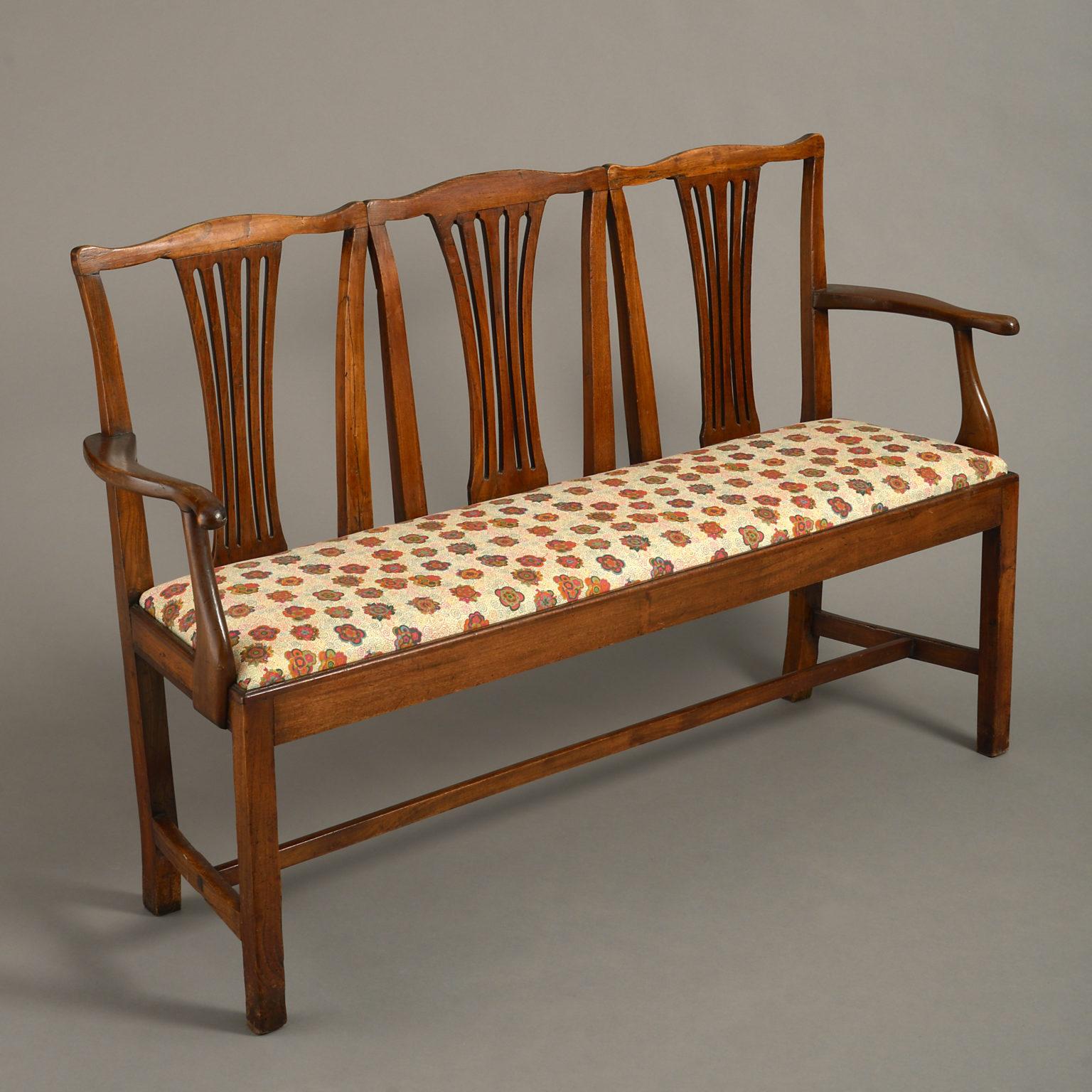 A late 18th century elmwood triple settee of rich color, the three pierced splats between shaped arms, having a drop in upholstered seat and raised on square block legs with an H-form stretcher.