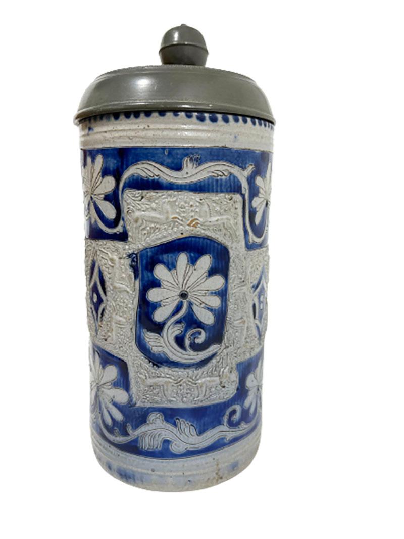 An 18th Century German Westerwald Salt Glazed Stoneware with Horses Tankard

A German Westerwald tankard with pewter engraved lid. The salt-glazed stoneware has horses and floral motifs in panels on a cobalt blue background. 
The tankard is from