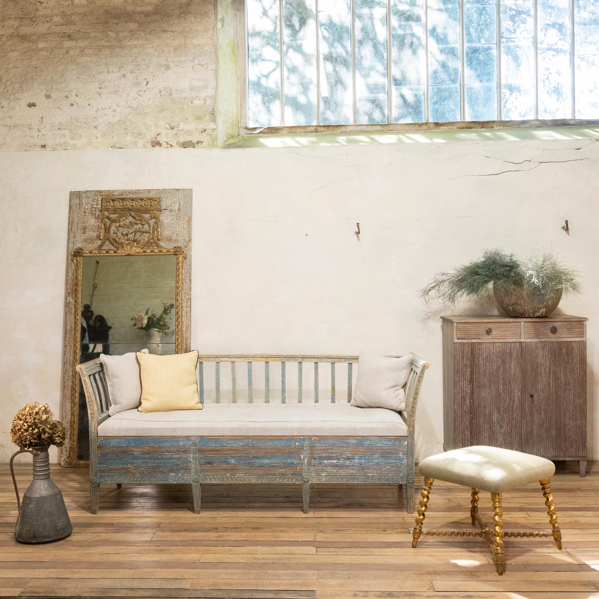 A striking 18th-century Swedish sofa - bench, displaying dry scraped original blue paint. Demonstrating gracefully splayed arms with elegant spindles to the back, displaying carved detailing throughout. The sofa features a pull out base - ideal for