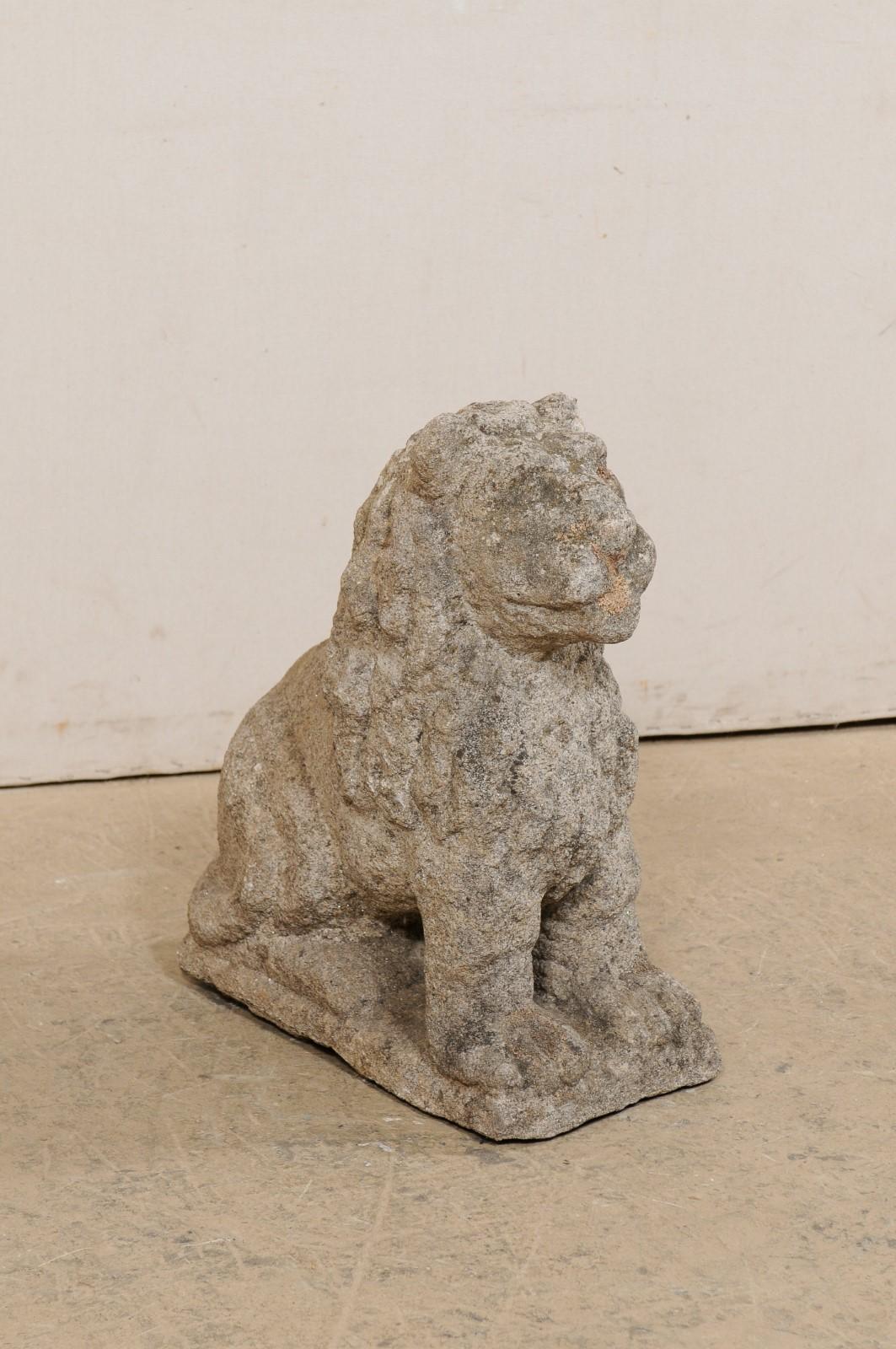 A European carved stone lion garden statue from the 18th century. This antique sculpture from Europe has been hand-carved in the image of a male lion, with long, wavy mane and resting in a sitting position, with head facing forward and tail curled