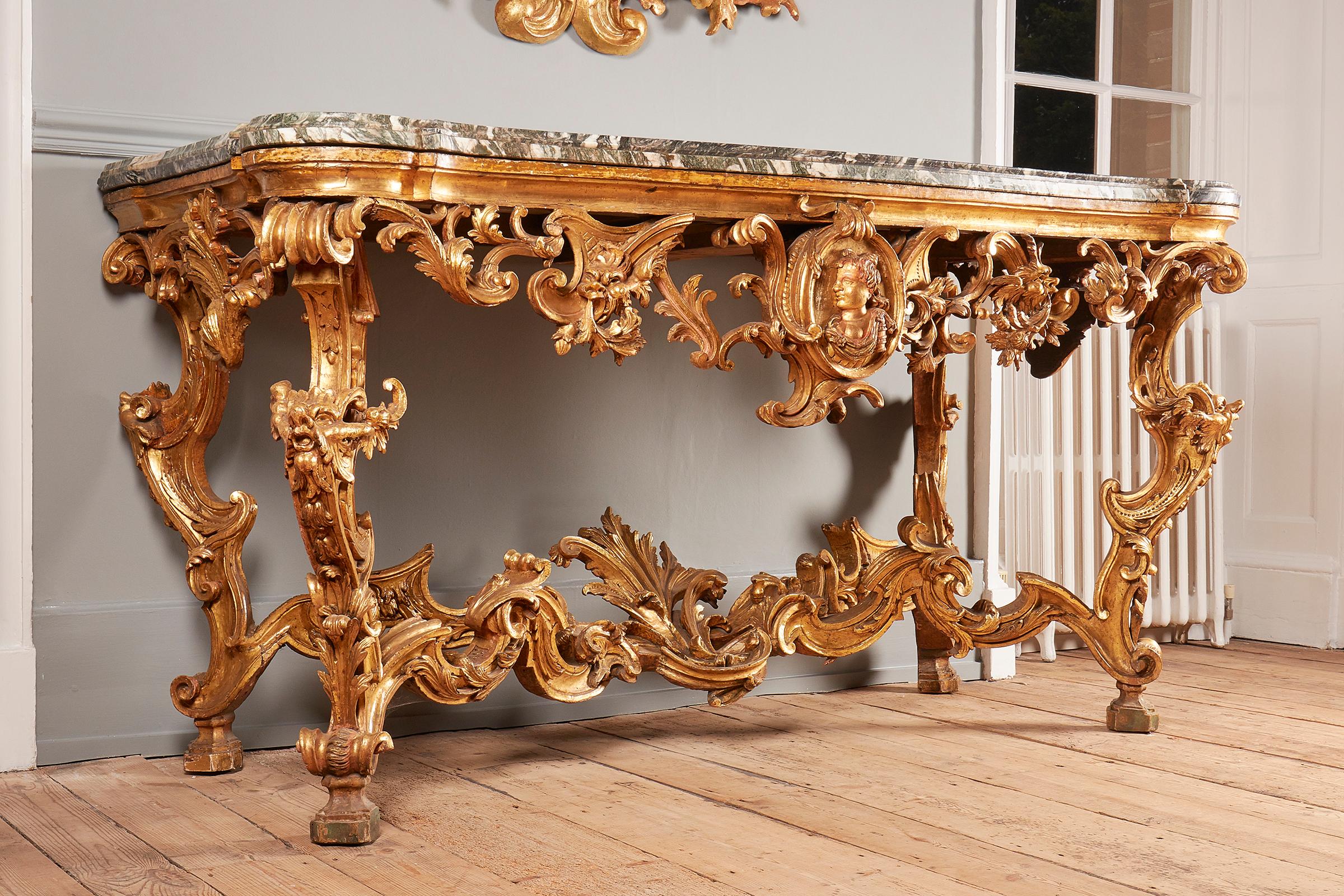 A fine Italian giltwood console table, Tuscany, second quarter of 18th century, serpentine-fronted, white-veined green cipollino marble top with rounded corners, a pierced foliate scrolling frieze with medallion with a female, above S-shaped legs