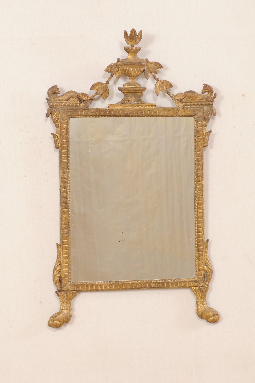 An Italian neoclassical carved and giltwood mirror from the 18th century. This antique mirror from Italy features a richly carved giltwood surround, in typical neoclassical style, adorn with a raised urn crest at top center of frame, with various