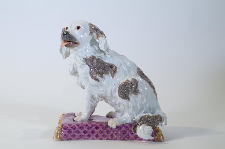 An 18th century Louis XVI period Meissen porcelain model of a King Charles spaniel, blue crossed swords mark, after the model by J.J. Kändler. The spotted dog with mouth open to reveal his tongue, seated on a gilt-tasseled diaper-pattern pillow.
