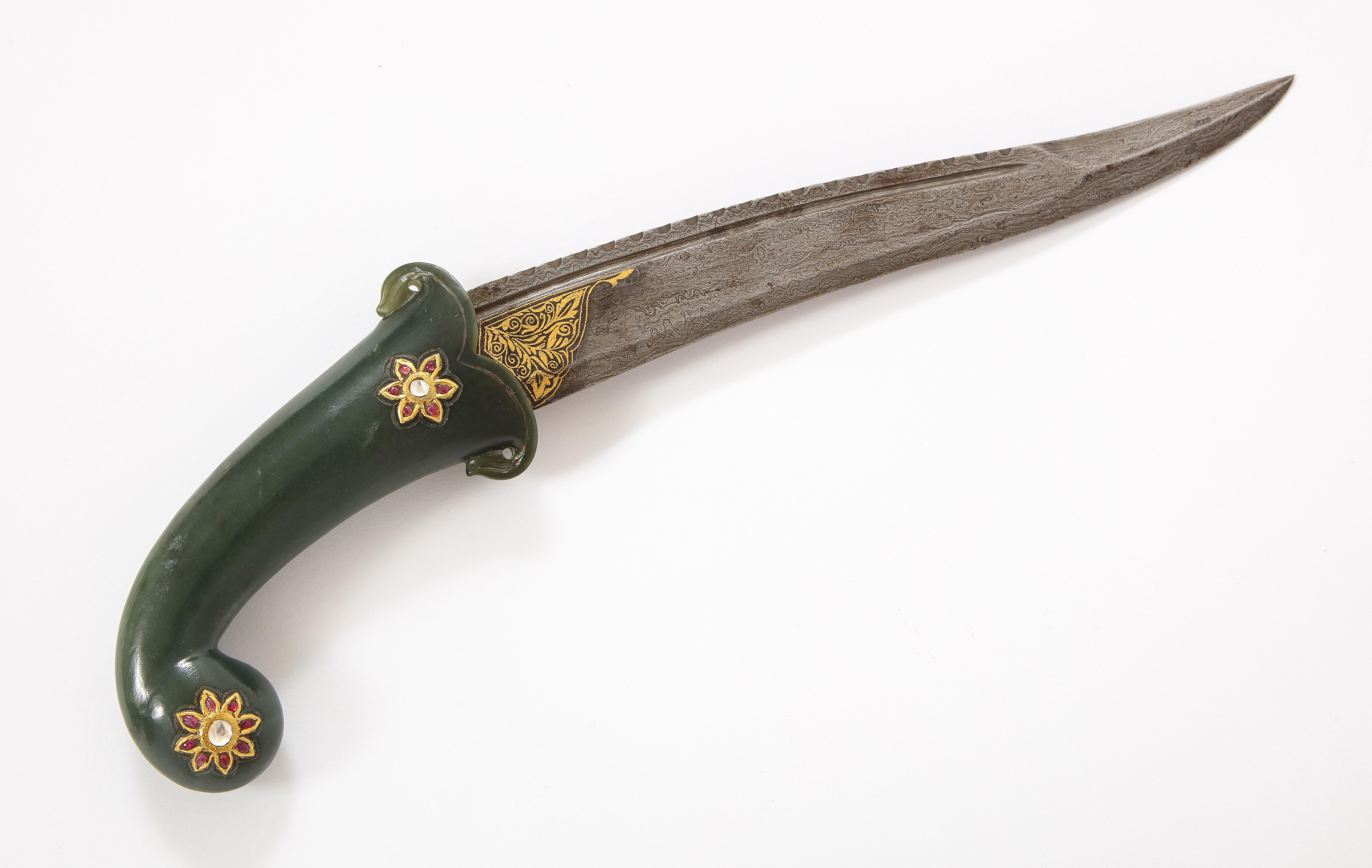 Gold- und edelsteinbesetzter Spinat-Jade-Dolch aus der Mogul-Dynastie mit einem dunkelgrünen Pistolengriff, der auf beiden Seiten mit Gold-, Rubin- und Saphirrosetten eingelegt ist. Die einschneidige Damastklinge hat einen gezackten Rücken und ein