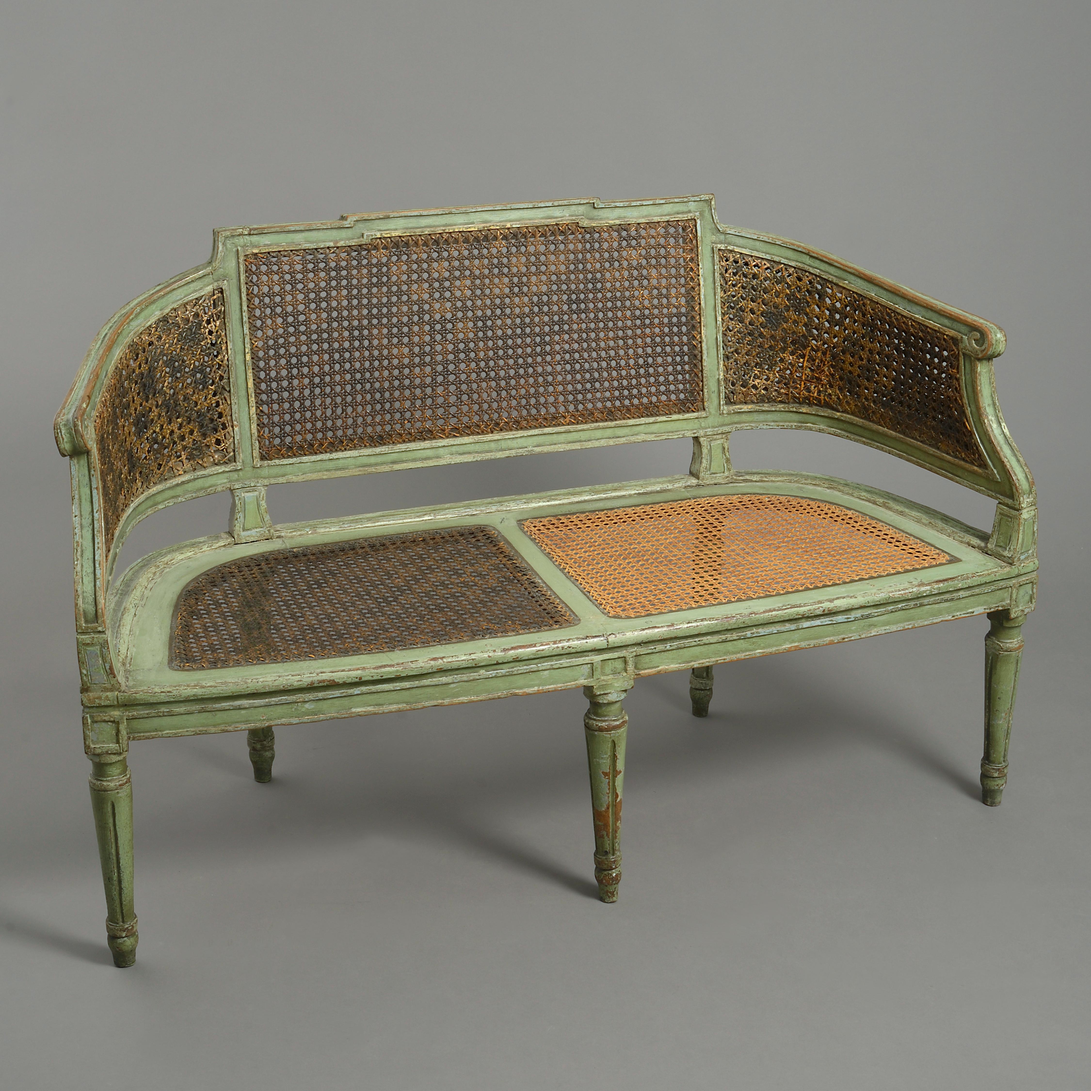 A late 18th century painted canapé sofa in the neoclassical taste, the green painted channeled frame with caned back and seat panels and raised upon turned tapering fluted legs. Having a drop in seat.
  