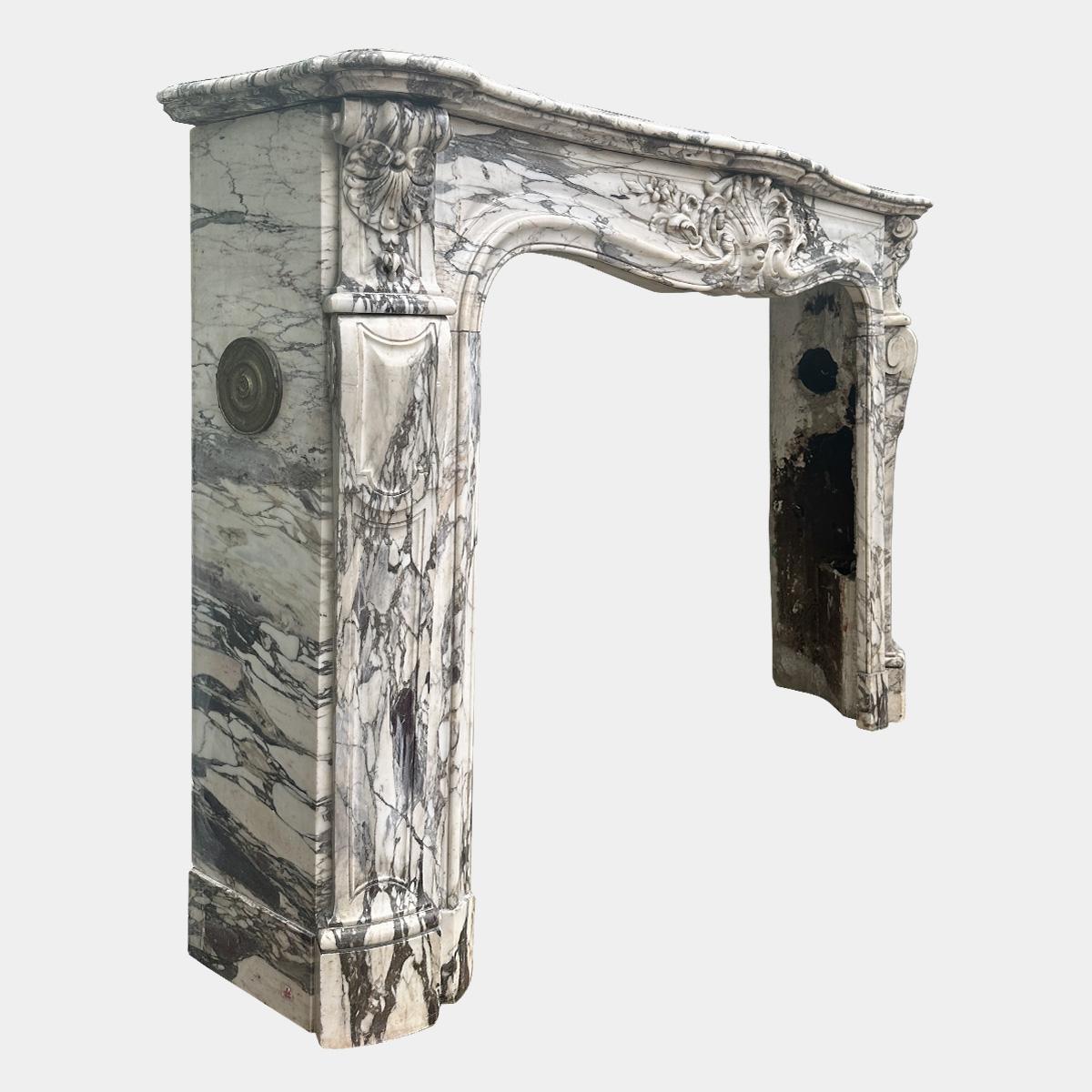 A  grande cheminée d'époque Louis XV exécutée en marbre de Brèche Violette de qualité supérieure. Les jambages avec de profonds retours latéraux conservent leurs évents en laiton d'origine, les panneaux avant sont cannelés et lambrissés avec des