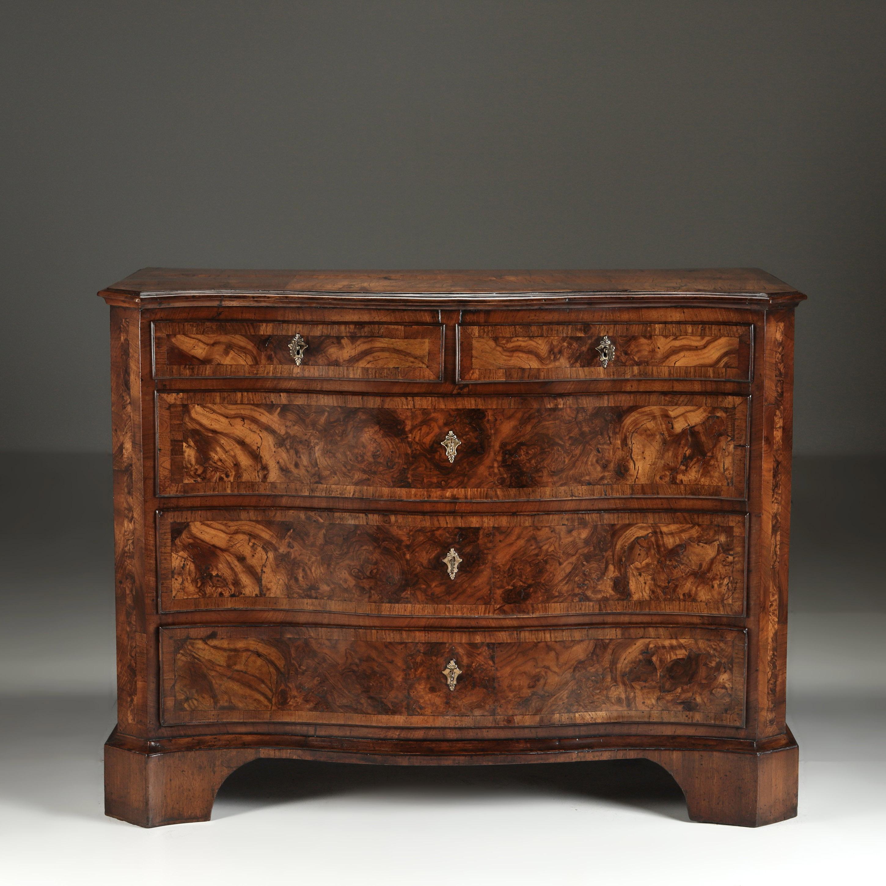 A Richly figured walnut veneered chest of three long and two short drawers, the whole framed with cross banding, raised on bold bracket feet.

The choice walnut timbers uninterrupted by handles, each opening on a key.
