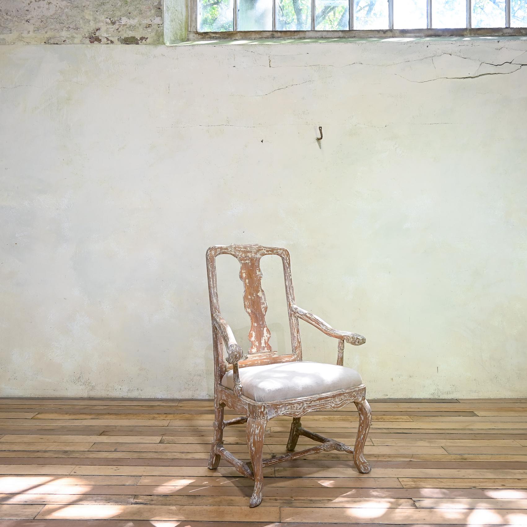 an 18th century Swedish open armchair displaying dry scraped paint. Featuring a pierced splat back, raised on, cabriole legs, united by a cross stretcher. A rectangular padded inset seat uphoslestered in a period linen. Flanked by splaying arms with
