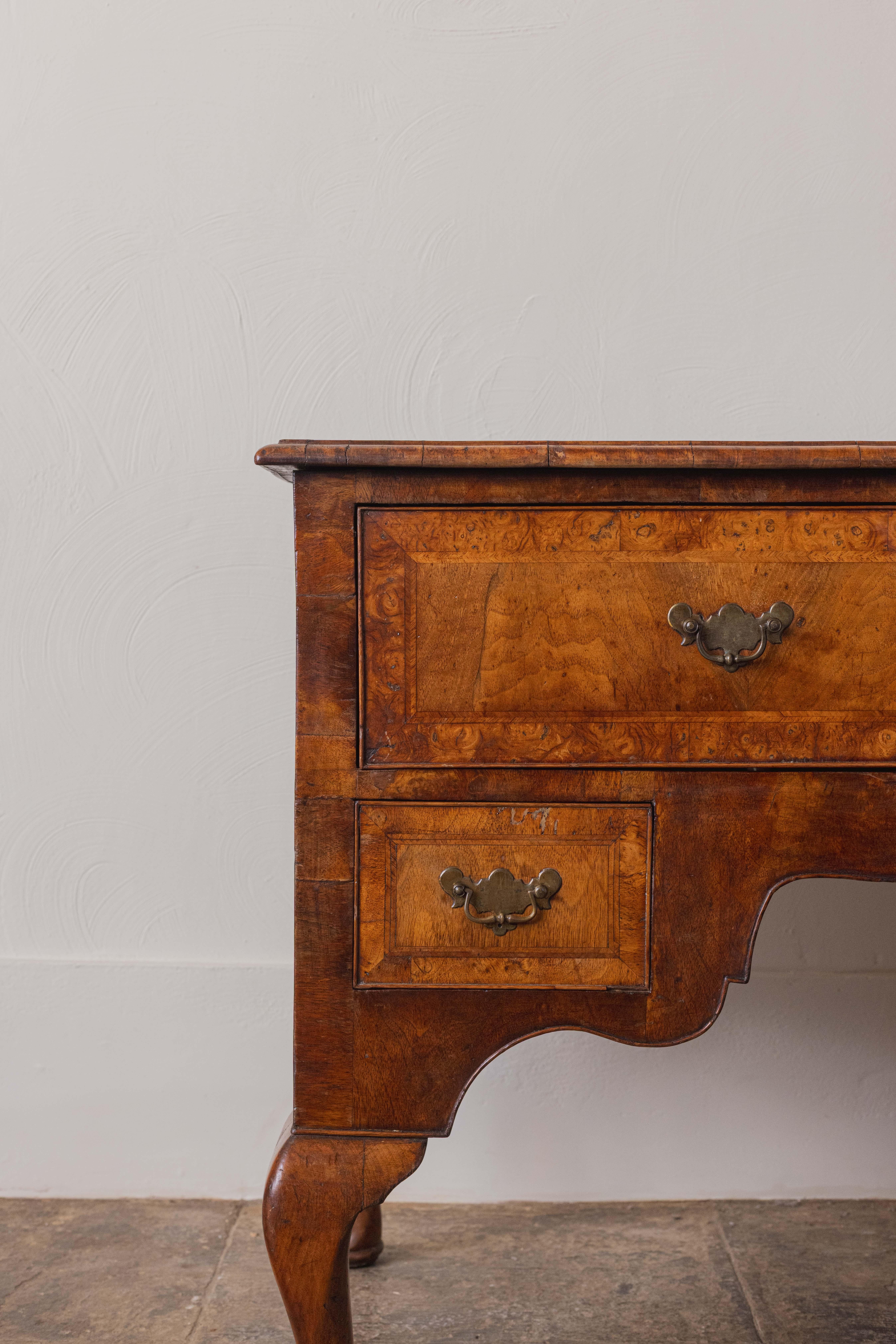 An elegant Queen Anne lowboy in richly figured burr walnut, retaining wonderful colour and patination. The rectangular top is quarter-veneered and cross-banded, over an arrangement of three drawers with original brass handles. The shaped apron and
