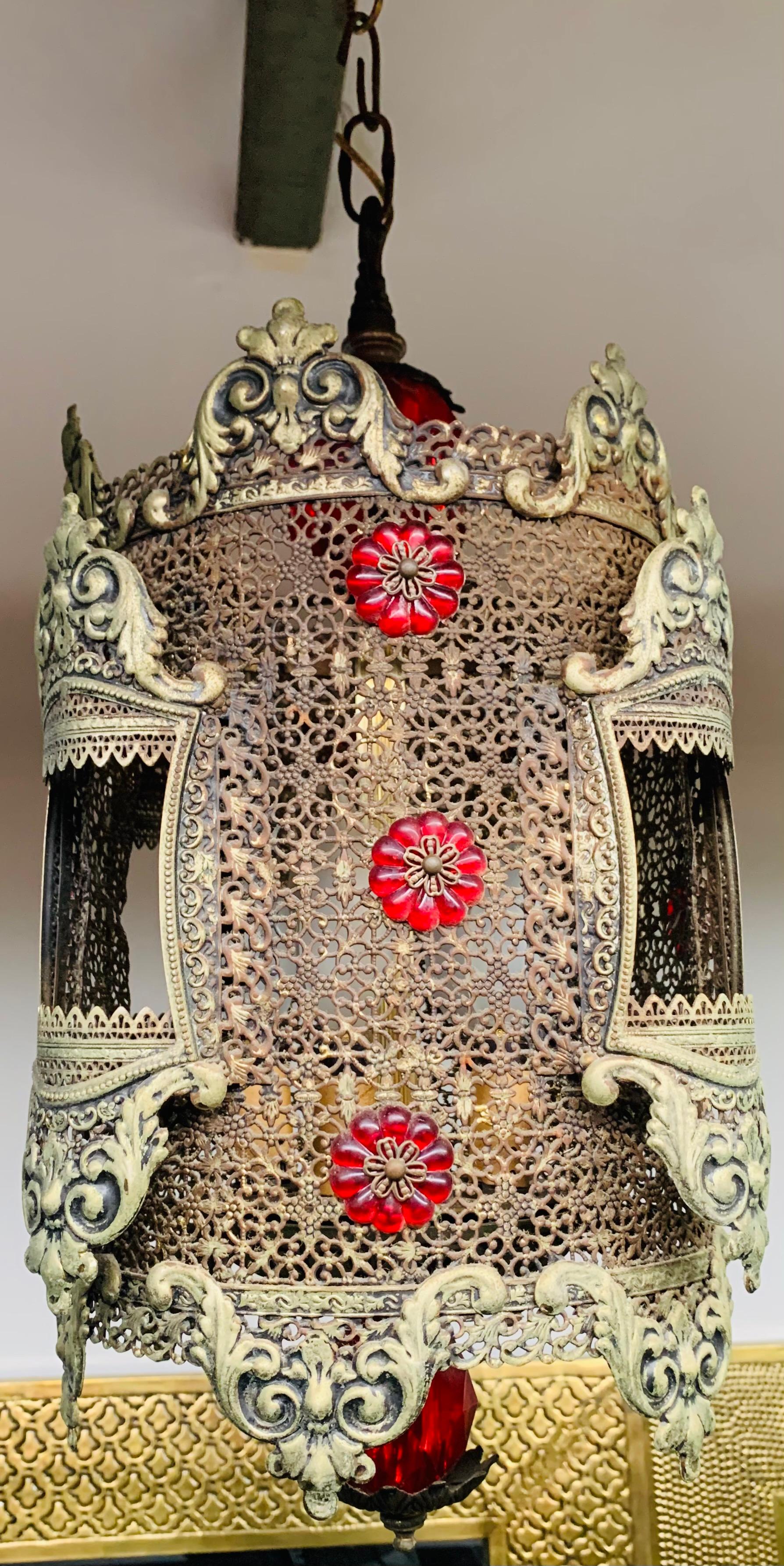 A decorative 1970s oriental style hanging gilt metal lantern or pendant. The cylindric shaped lantern features decorative red faux crystals and fine filigree design. The lantern will add an exotic touch to any space. 

Dimensions: 13.5