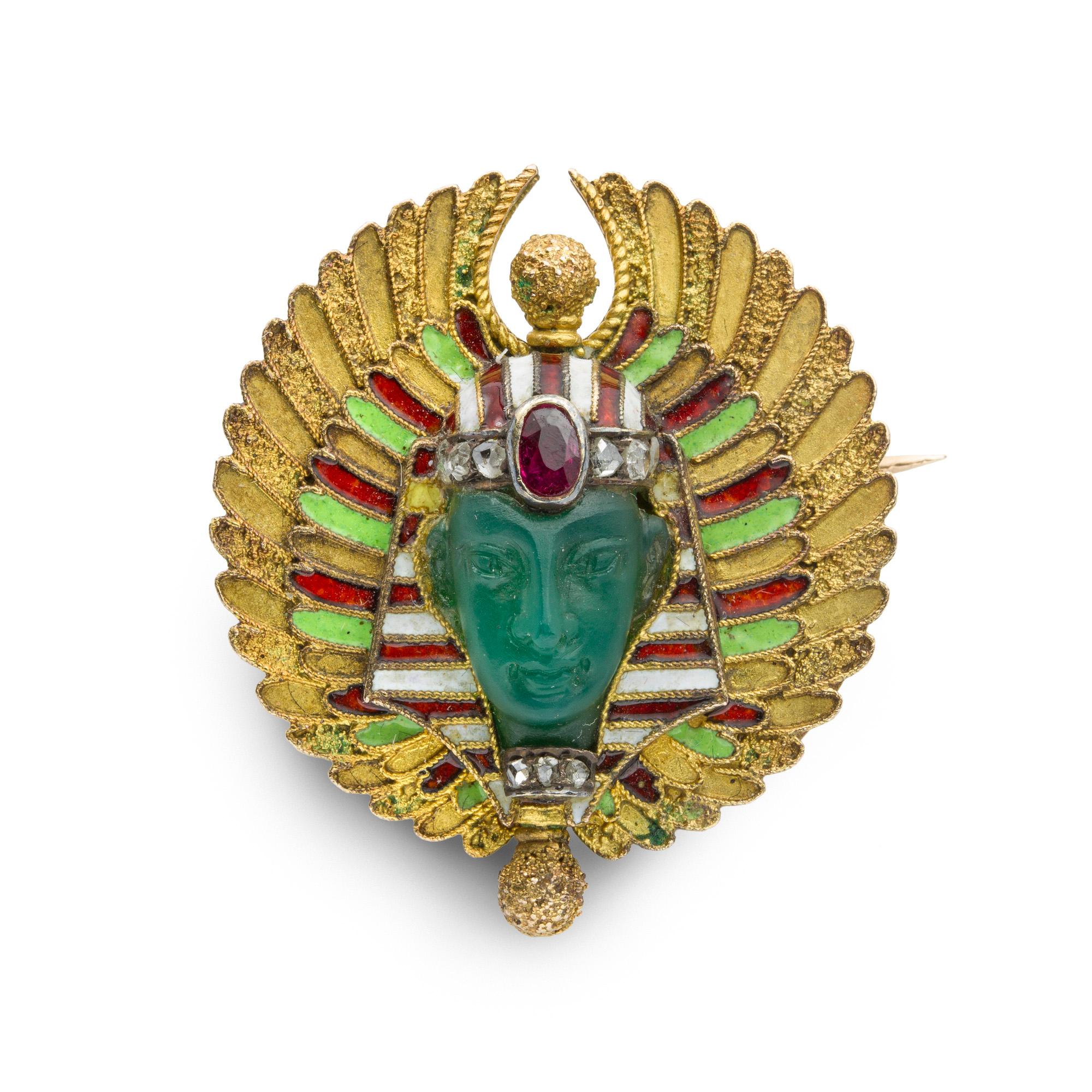 An 19th century Egyptian revival Pharaoh brooch, the chalcedony realistically carved as the face of the Pharaoh in a millegraine setting, wearing an oval faceted ruby and rose-cut diamond-set band on his forehead surrounded by a white and red enamel