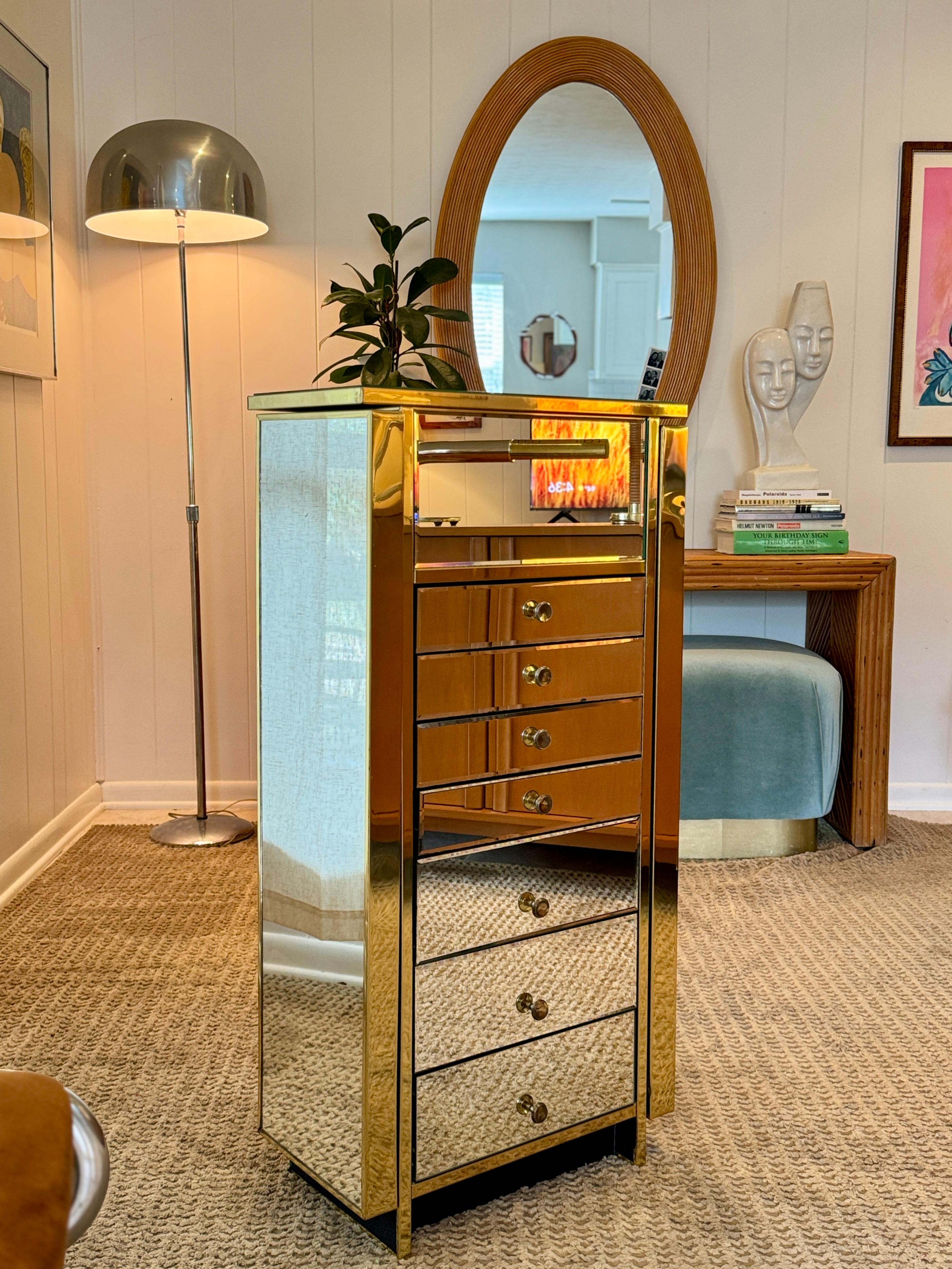 An absolutely fabulous mirrored armoire or jewelry case, with brass borders and pulls, circa 1970s. Features seven central drawers plus a larger mirrored top drawer, and two side doors designed for hanging necklaces. Overall, in very good